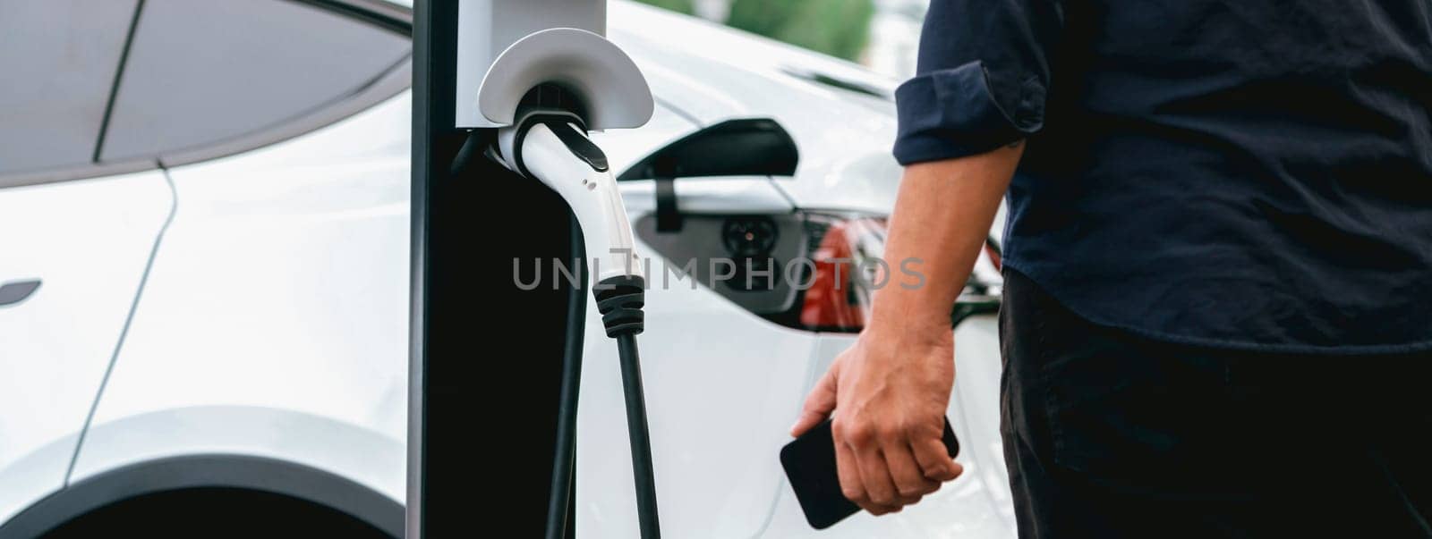 Man using smartphone to pay for electric car charging. Exalt by biancoblue