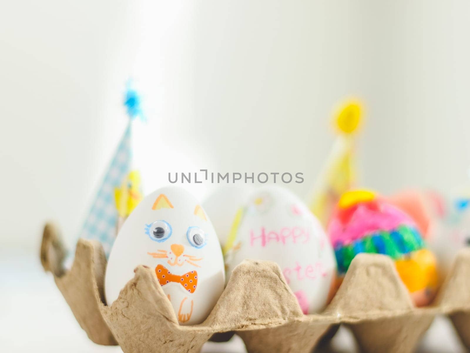 Cardboard package with decorated Easter eggs with glued and painted Easter bunny faces on a marble table with depth of field, side view. The concept of diy, crafts, children art, artisanal, handicraft, diy.