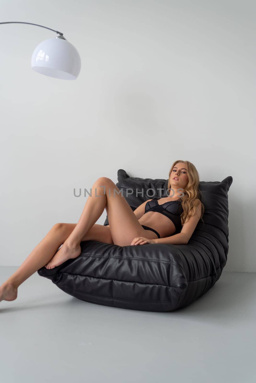 Beautiful young blonde woman in black lingerie posing on grey background