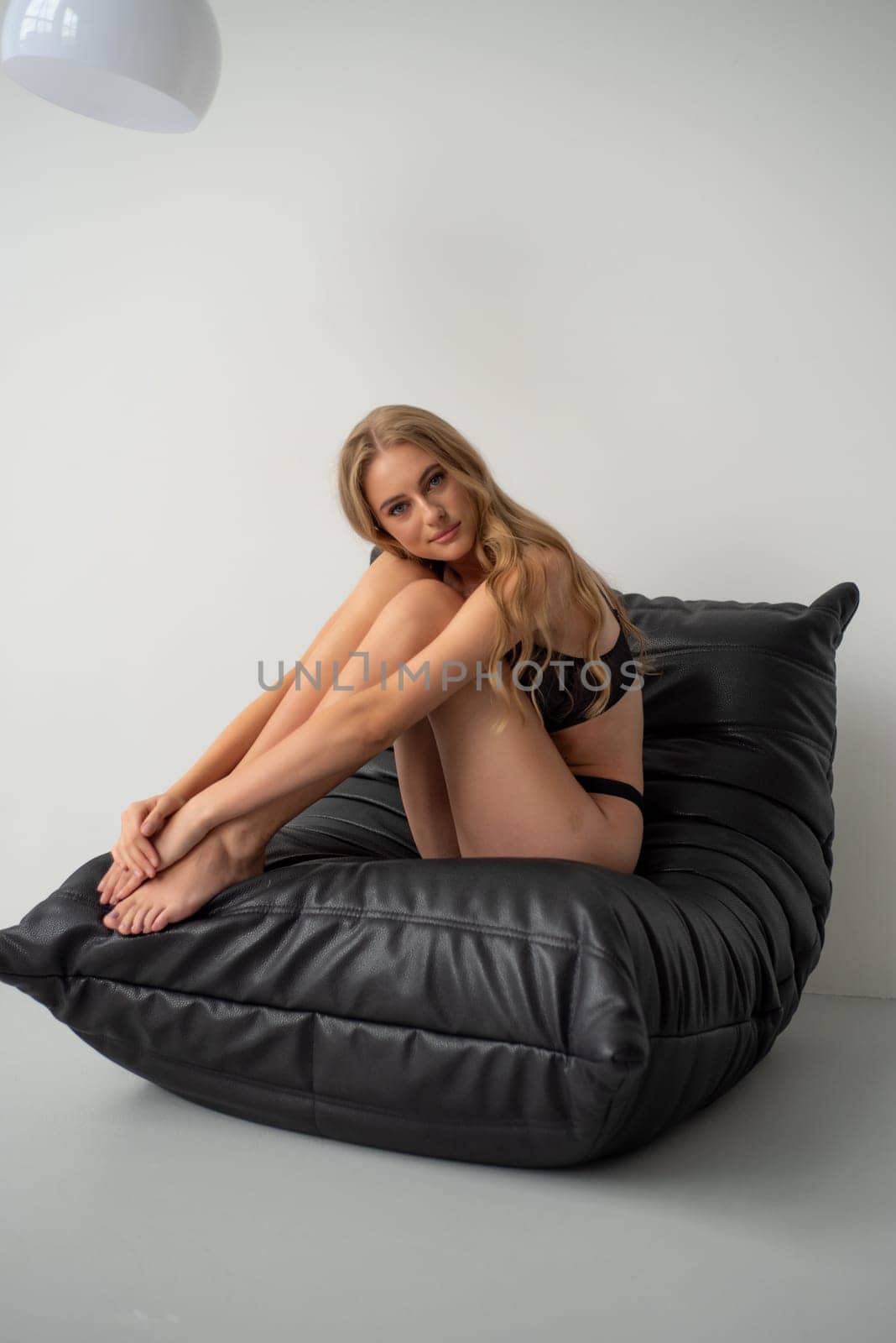 Beautiful young blonde woman in black lingerie posing on grey background