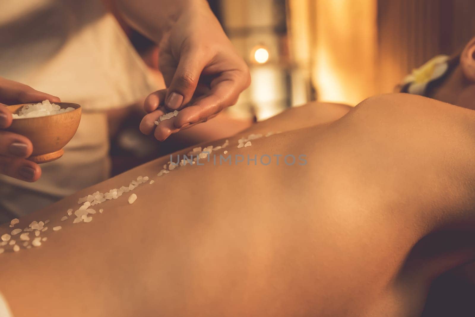 Closeup couple customer having exfoliation treatment in luxury spa salon with warmth candle light ambient. Salt scrub beauty treatment in Health spa body scrub. Quiescent