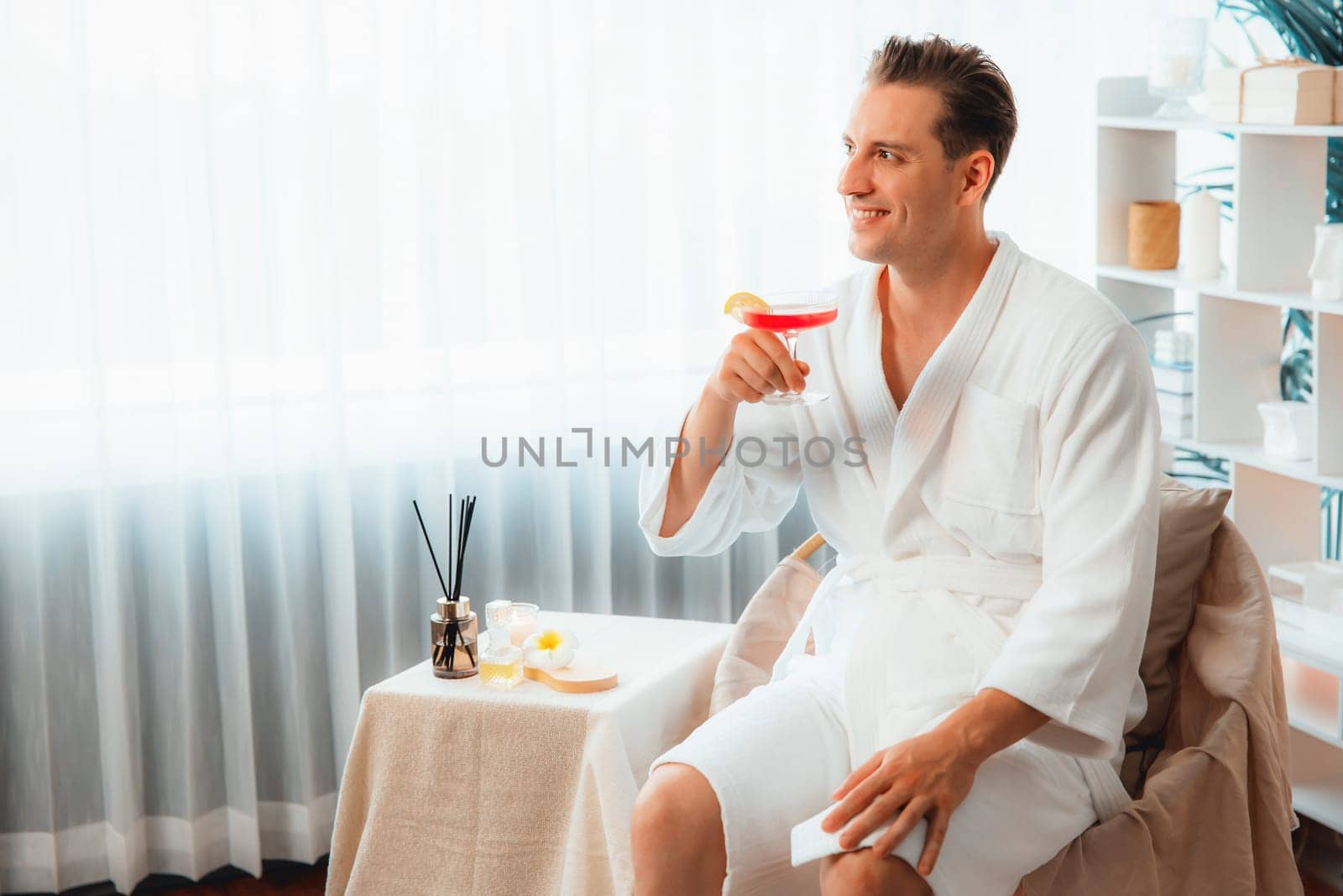 Beauty or body treatment spa salon vacation lifestyle concept with man wearing bathrobe relaxing with drinks in luxurious hotel spa or resort room. Vacation and leisure relaxation. Quiescent