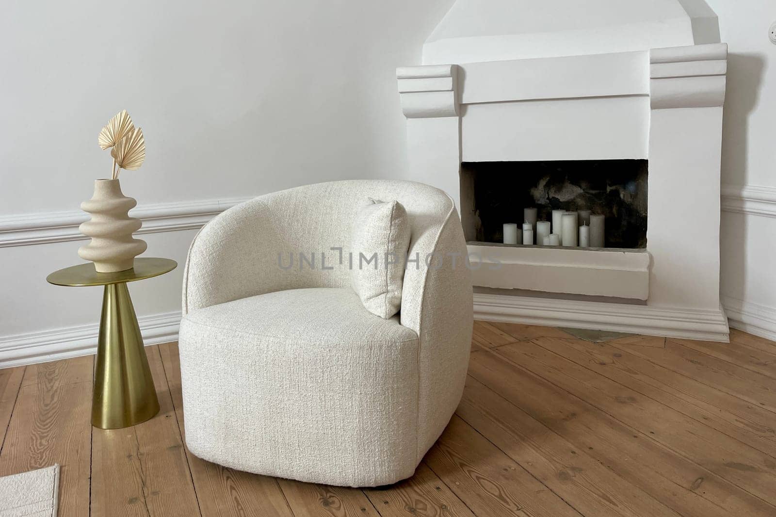 A soft chair and a decorative vase in a beige room on the background of a fireplace. High quality photo