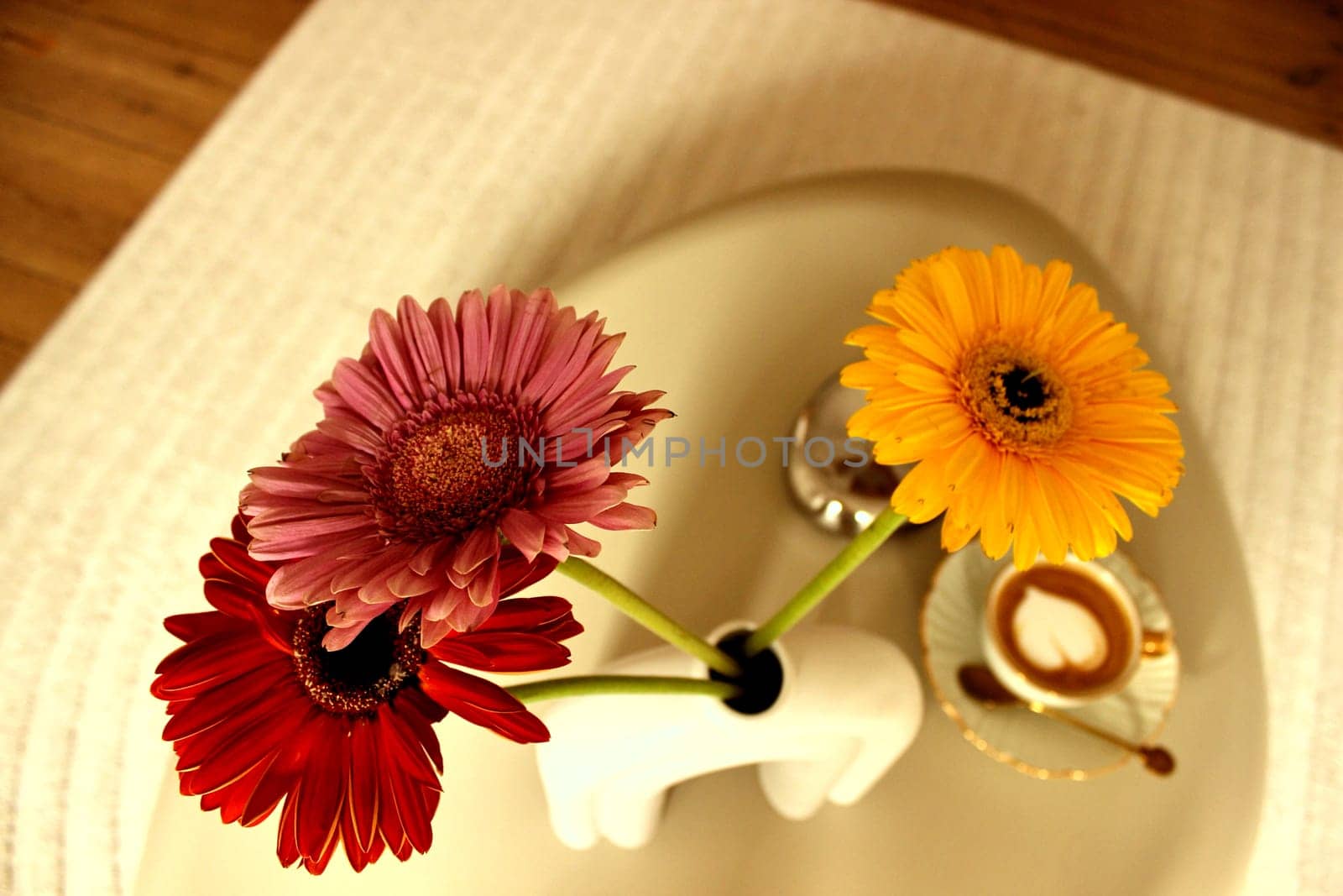 Gerbera flowers and a cup of coffee on a table in a beige bedroom. High quality photo