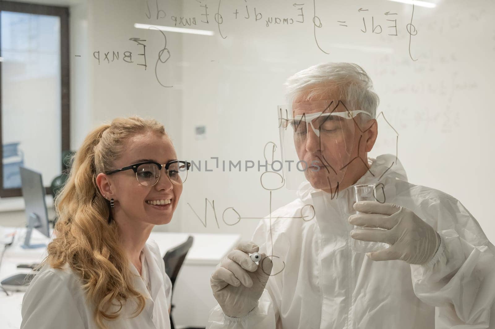 Two chemist colleagues write formulas on glass. Caucasian elderly man and young woman brainstorming