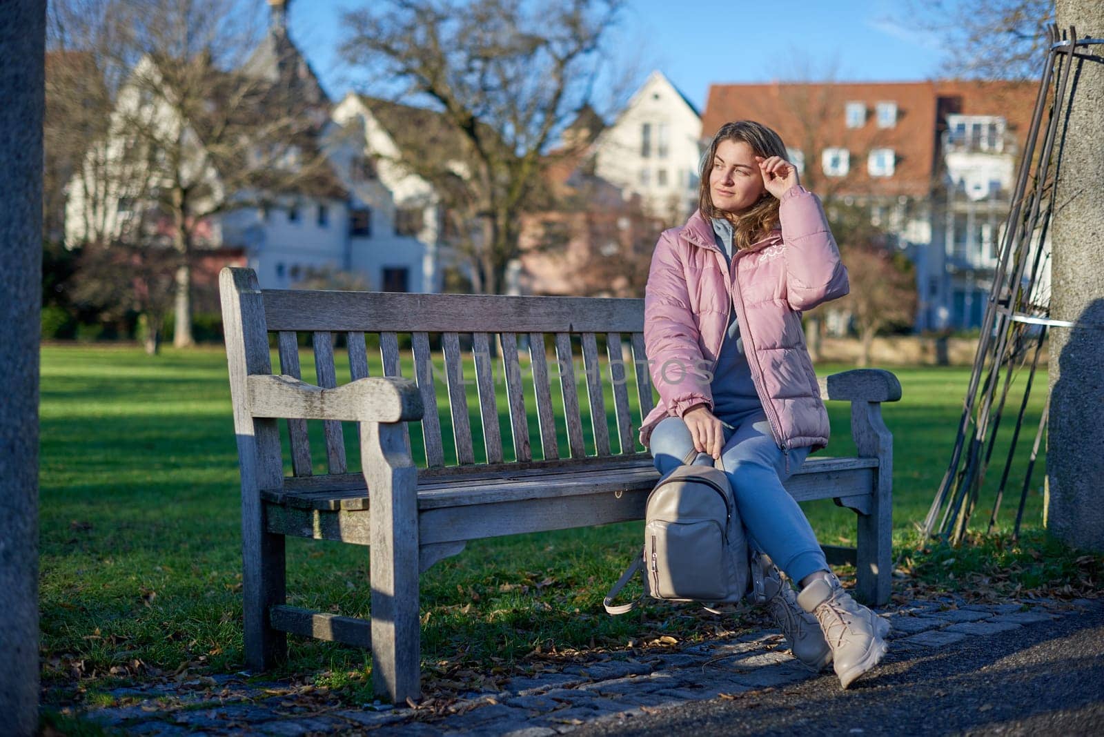 Winter Joy in Bitigheim-Bissingen: Beautiful Girl in Pink Jacket Sitting Amidst Half-Timbered Charm. beautiful girl in a pink winter jacket sitting on a bench in a park, set against the backdrop of the historic town of Bitigheim-Bissingen, Baden-Württemberg, Germany. by Andrii_Ko