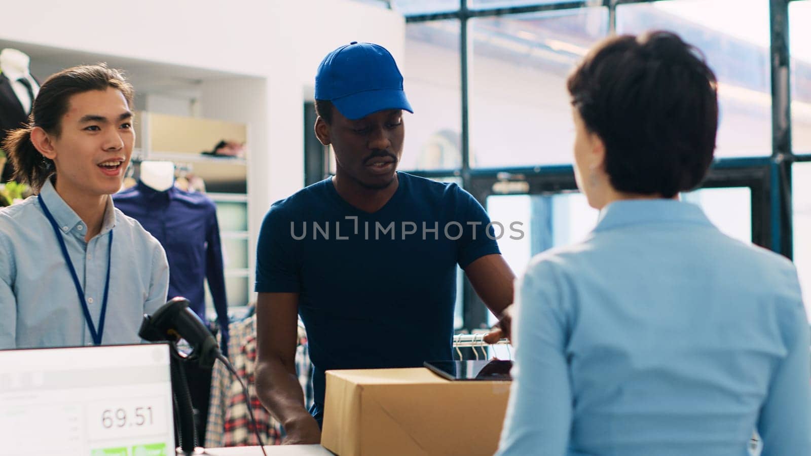 Courier in delivery uniform in modern boutique, discussing packages shipping details with store manager. African american deliveryman showing distribution report on tablet computer. Fashion concept