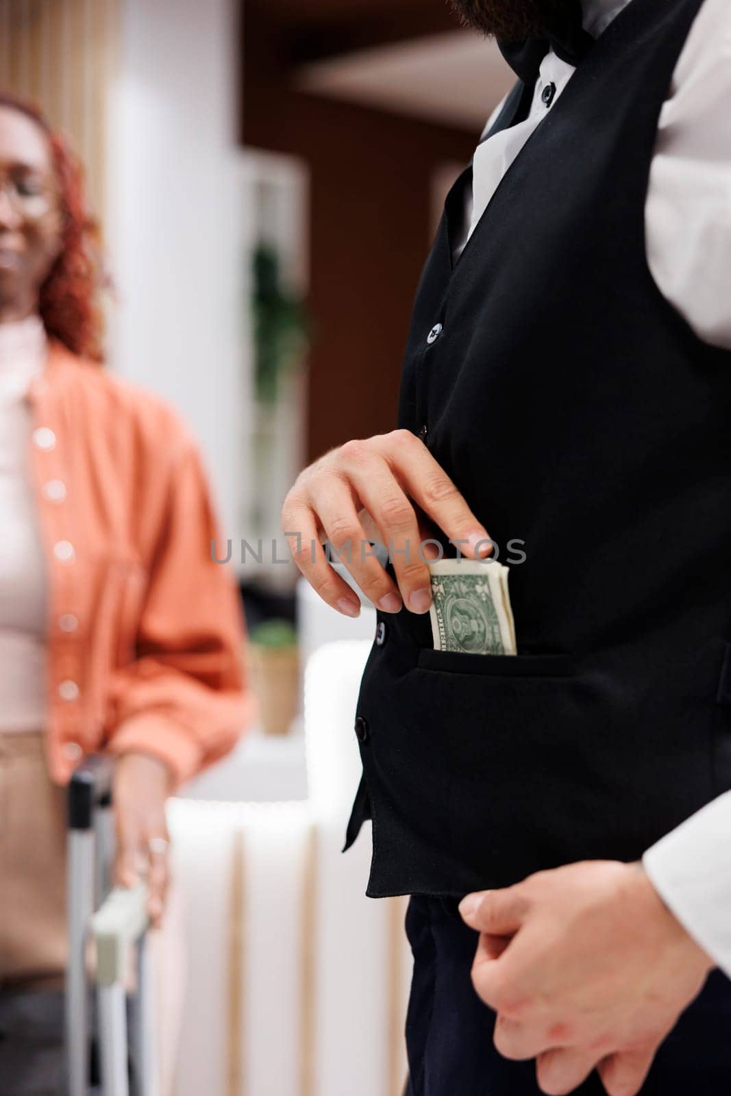 Bellboy accepting cash from people, putting money in pocket and carrying suitcases for hotel guests. Male steward working as concierge taking tip from tourists, luxury service. Close up.