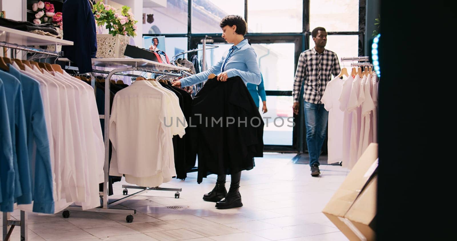 Cheerful employee arranging stylish clothes, working at modern boutique visual. Caucasian manager putting hangers with fashionable merchandise on racks in shopping centre. Fashion concept