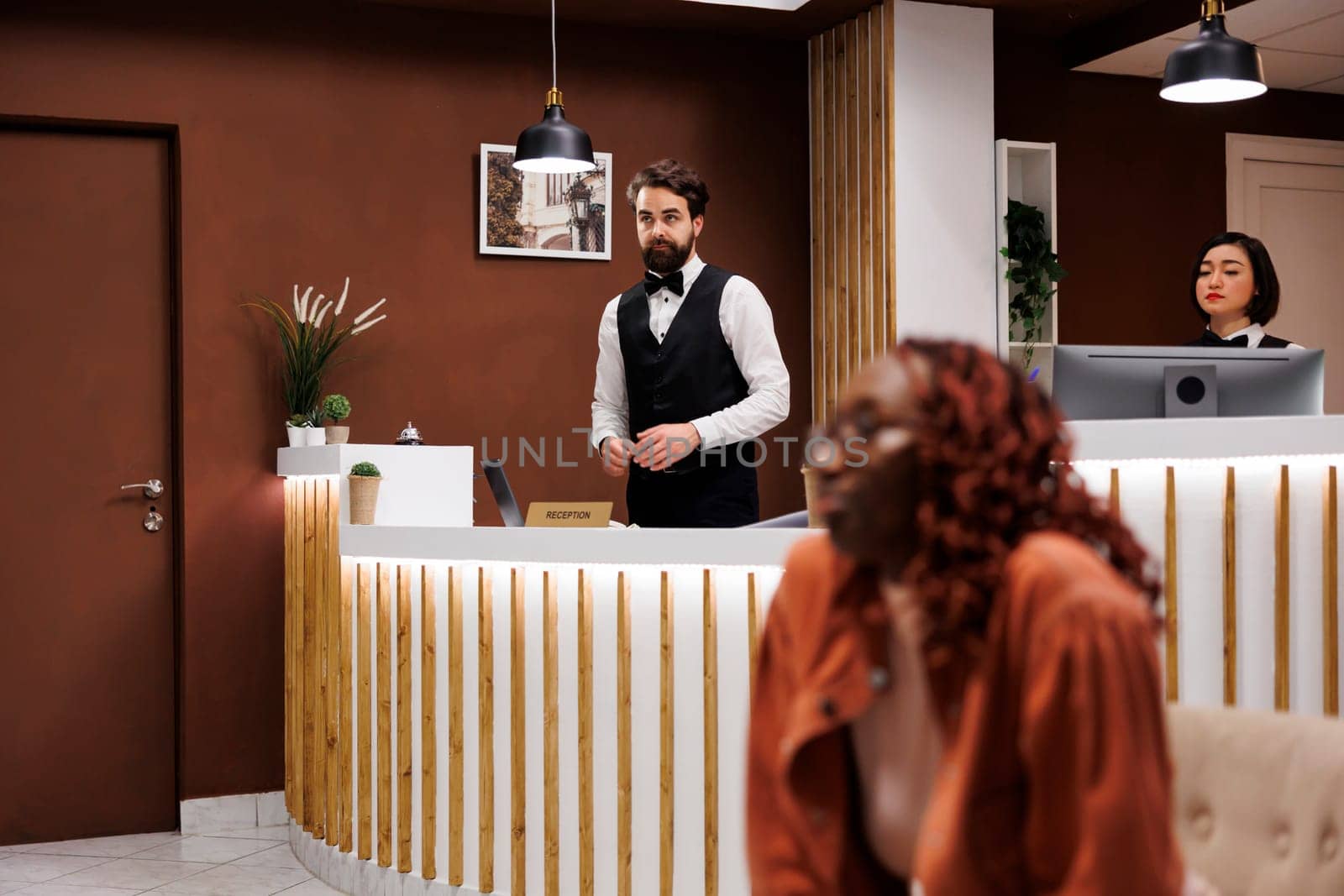 Hotel receptionist working at front desk, helping tourists with accommodation and great hospitality service. Male employee at lobby counter preparing to check in and check out guests.