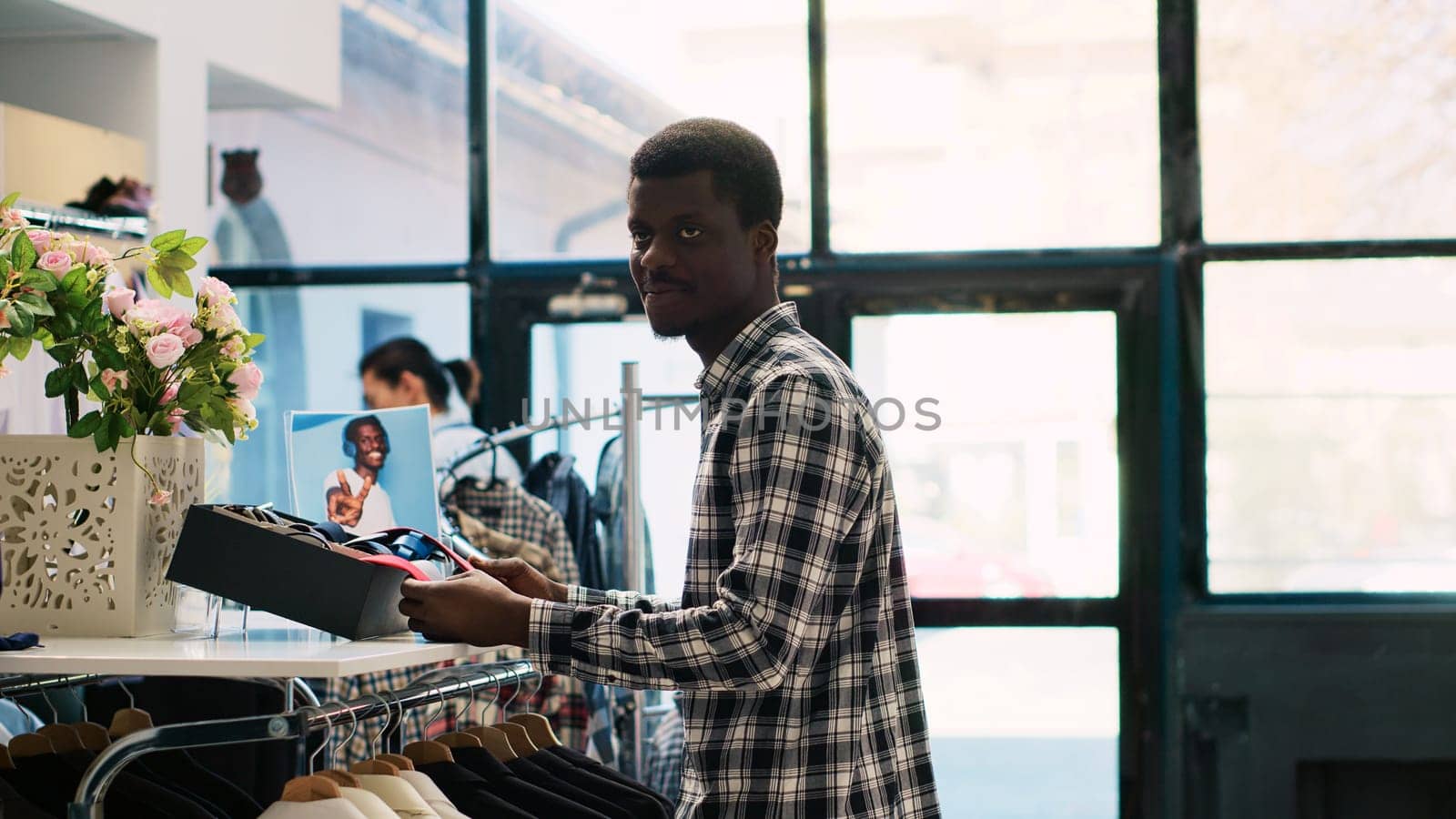 African american customer checking tie material, shopping for stylish accessories and merchandise in clothing store. Man client looking at shelf with new fashion collection in modern boutique