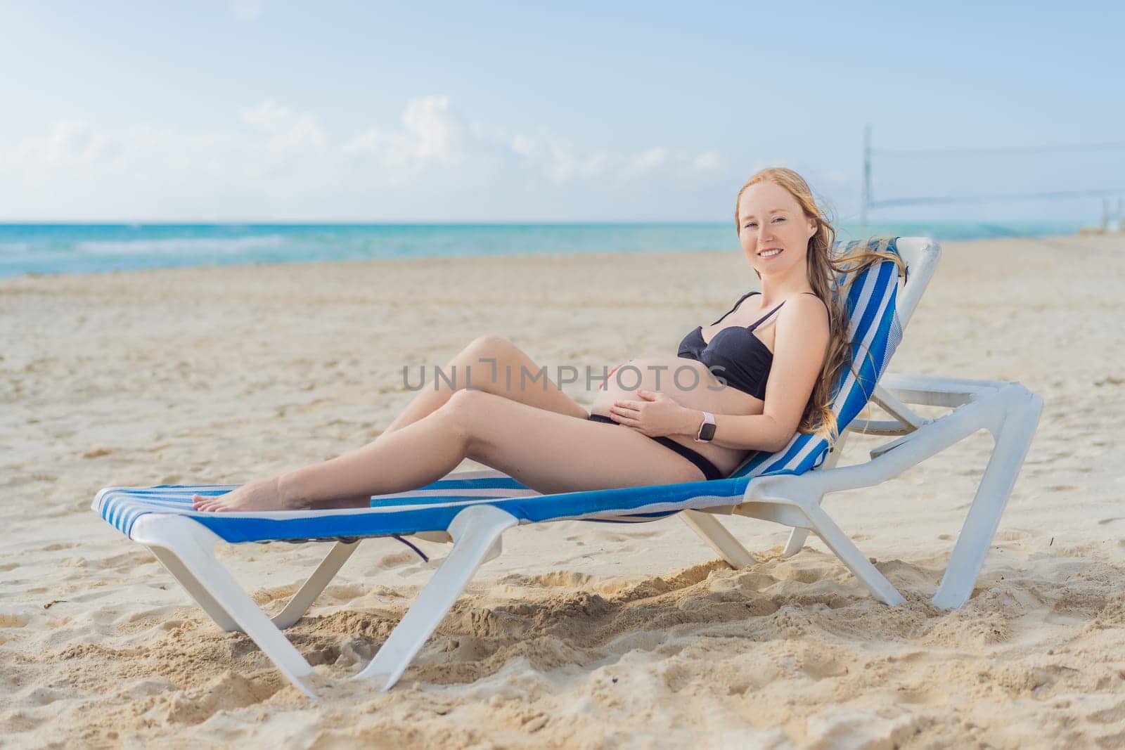 Basking in seaside tranquility, a pregnant woman lounges on a sun lounger, embracing the soothing ambiance of the beach for a moment of serene relaxation by galitskaya