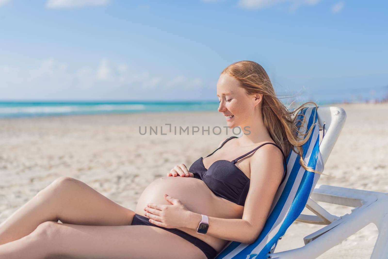 Basking in seaside tranquility, a pregnant woman lounges on a sun lounger, embracing the soothing ambiance of the beach for a moment of serene relaxation by galitskaya