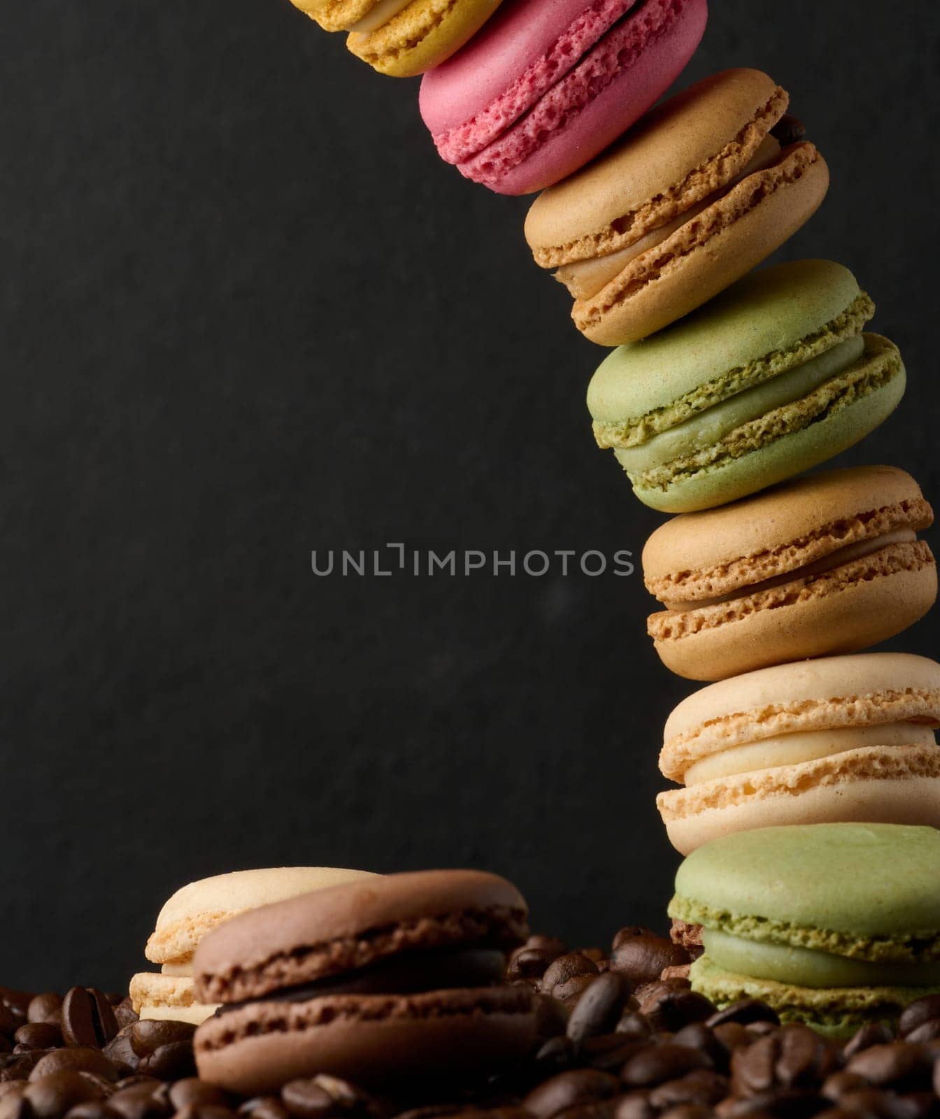 Stack of multi-colored macarons on a background of coffee beans, black background by ndanko