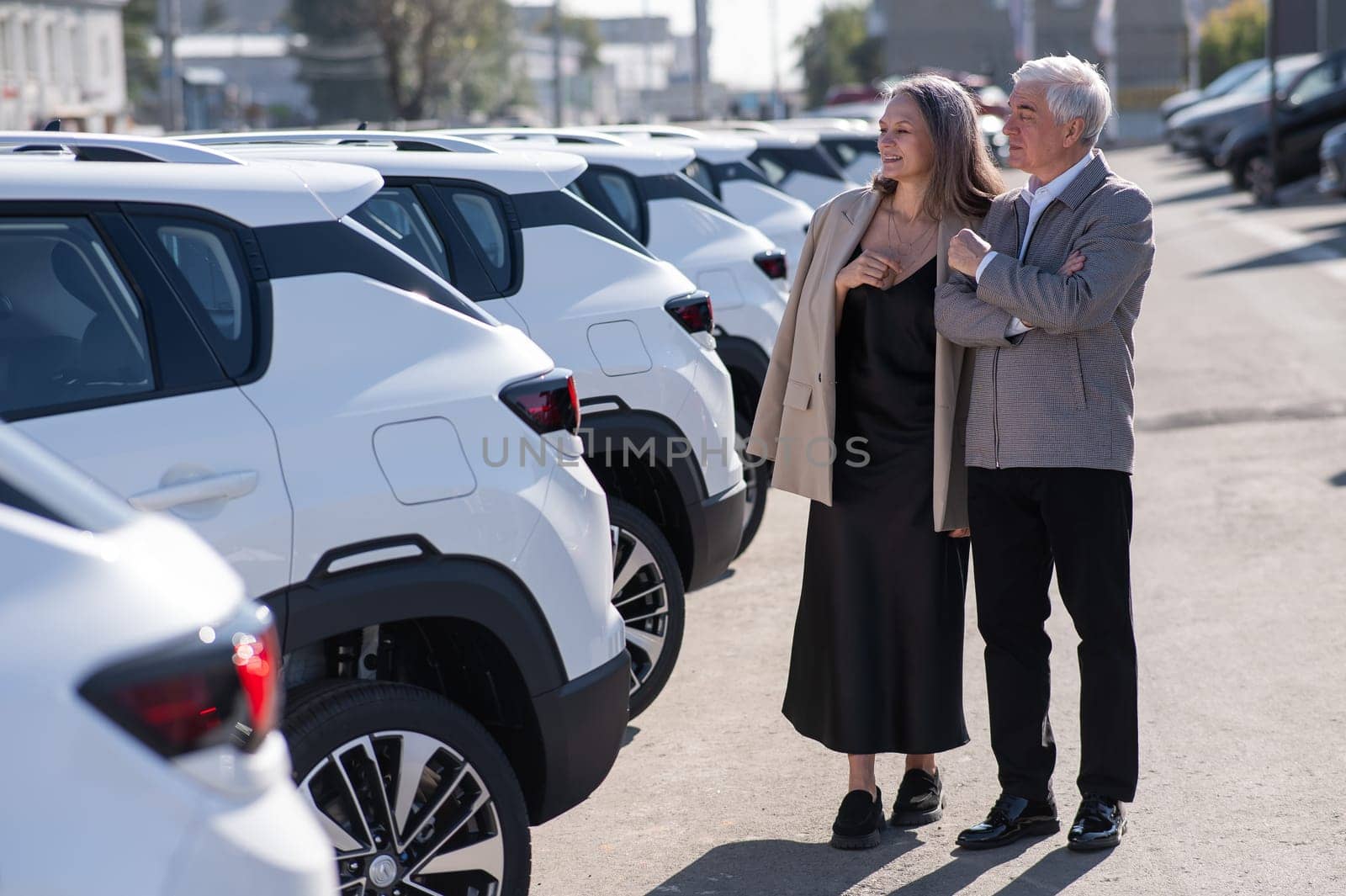 Mature Caucasian couple walks past cars outdoors, choosing a new one