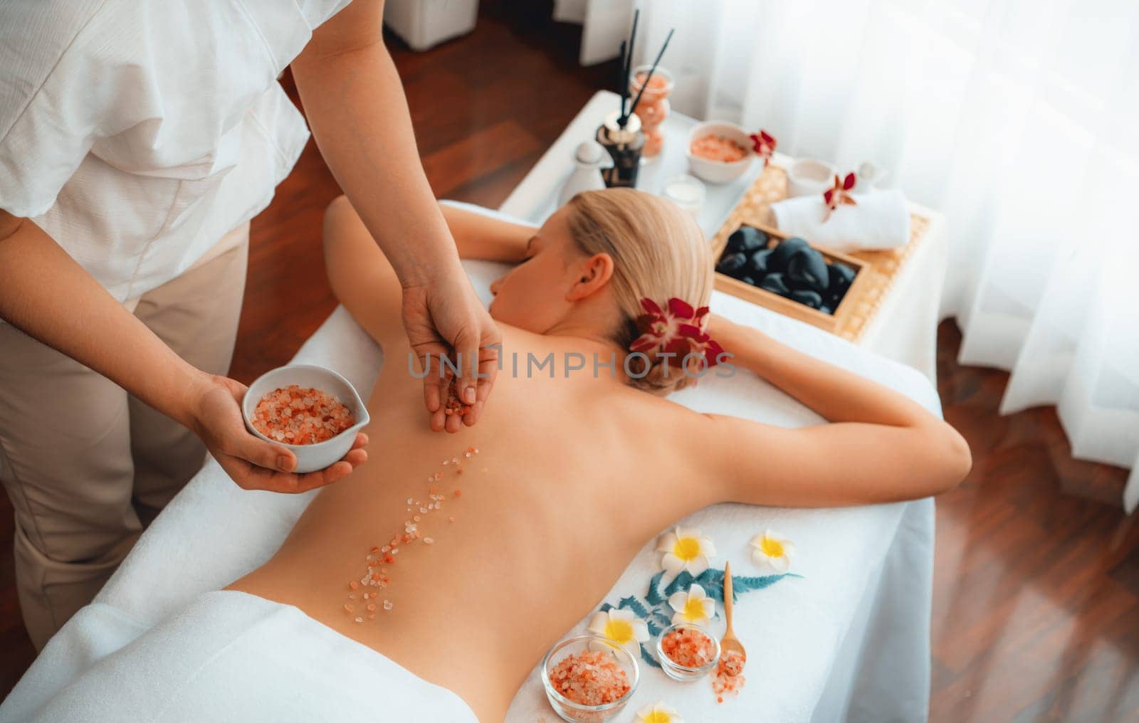 Woman customer having exfoliation treatment in luxury spa salon with warmth candle light ambient. Salt scrub beauty treatment in health spa body scrub. Quiescent