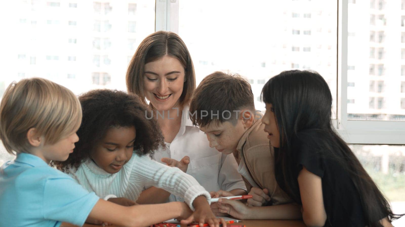 Professional caucasian teacher telling story to diverse student while sitting at table with storybook and colored book. Smart learner listening story while colored picture from instructor. Erudition.