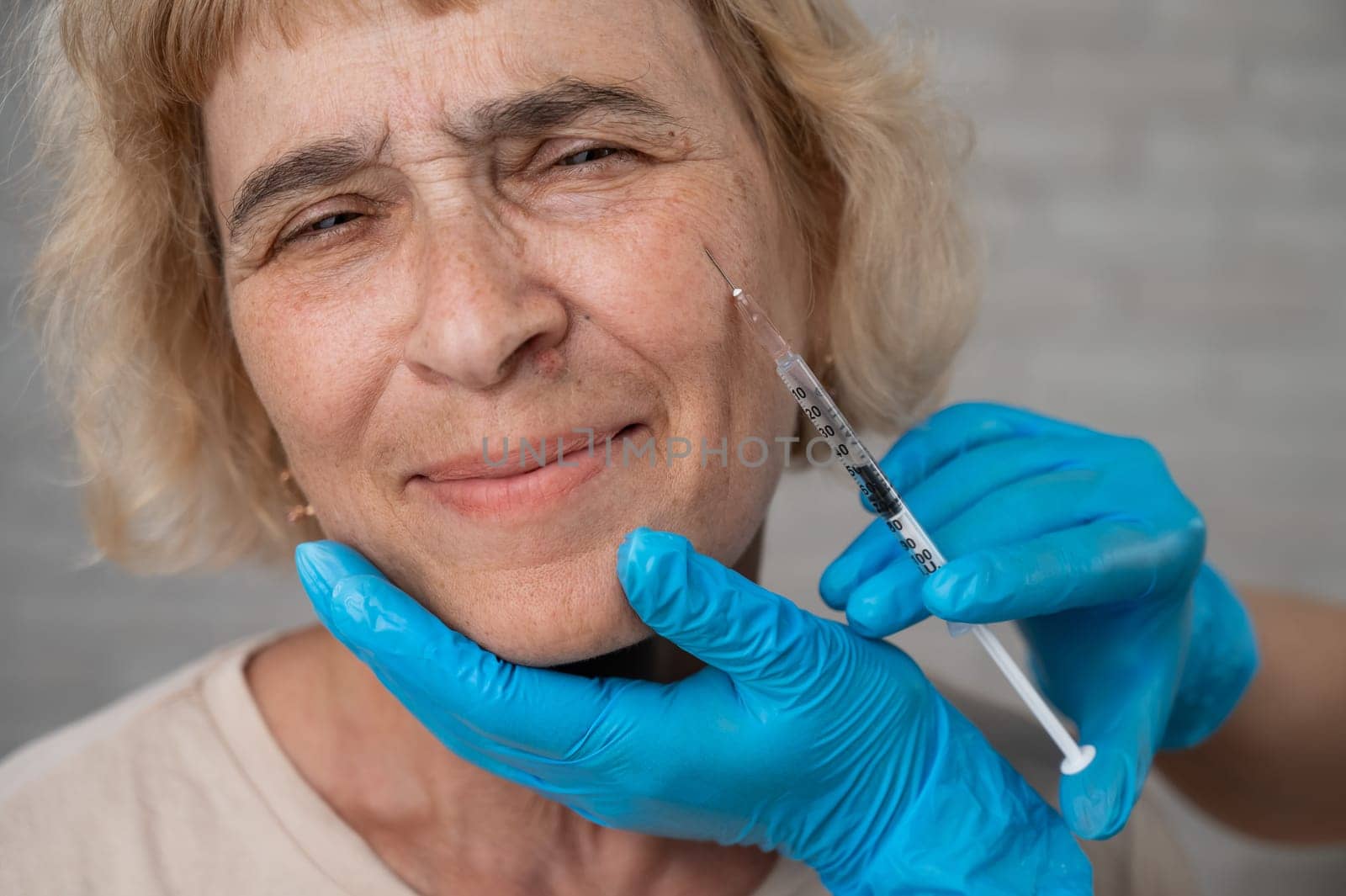 Doctor makes beauty injections in the face of an old caucasian woman