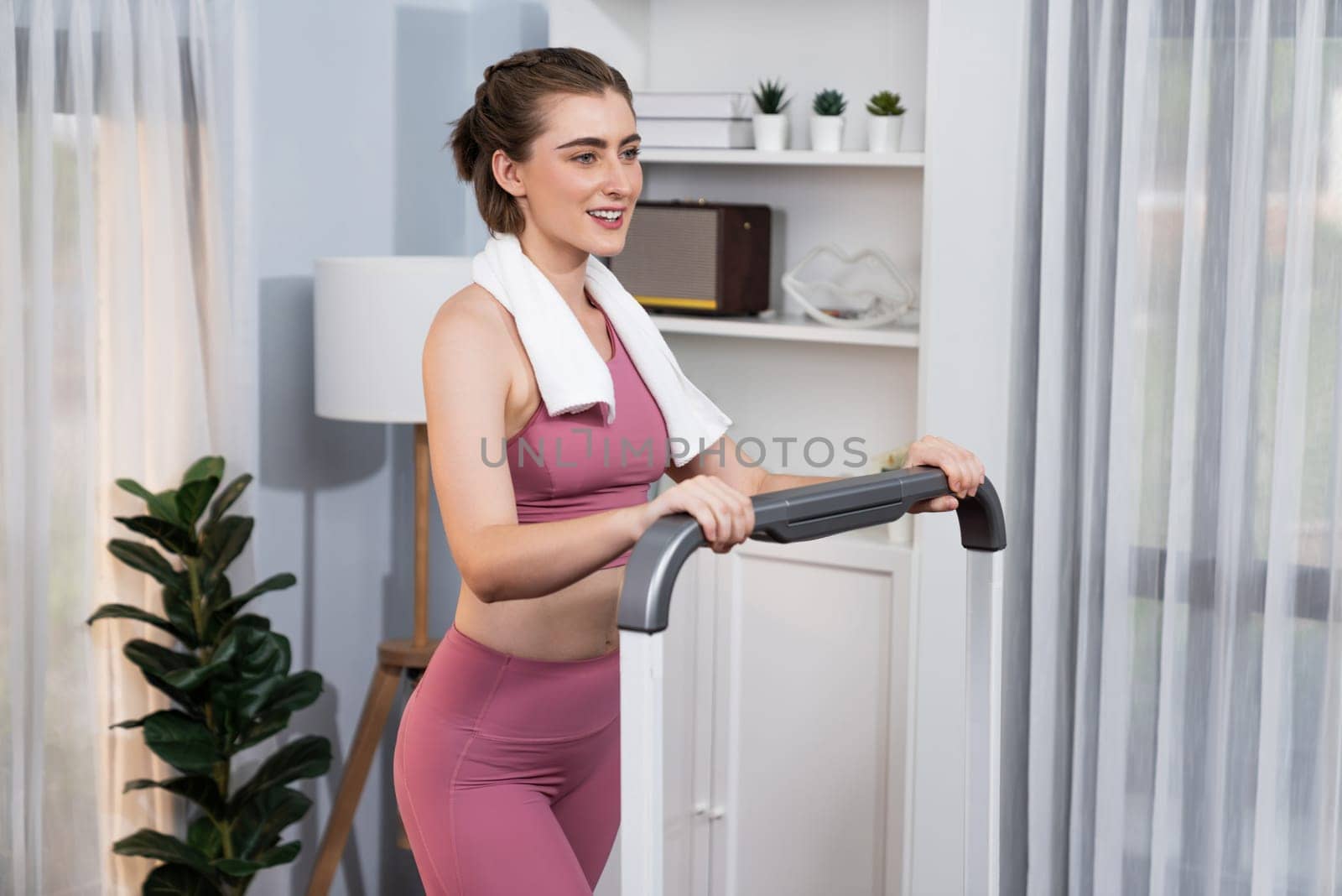 Athletic and sporty woman running on treadmill running machine during home body workout exercise session for fit physique and healthy sport lifestyle at home. Gaiety home exercise workout training.