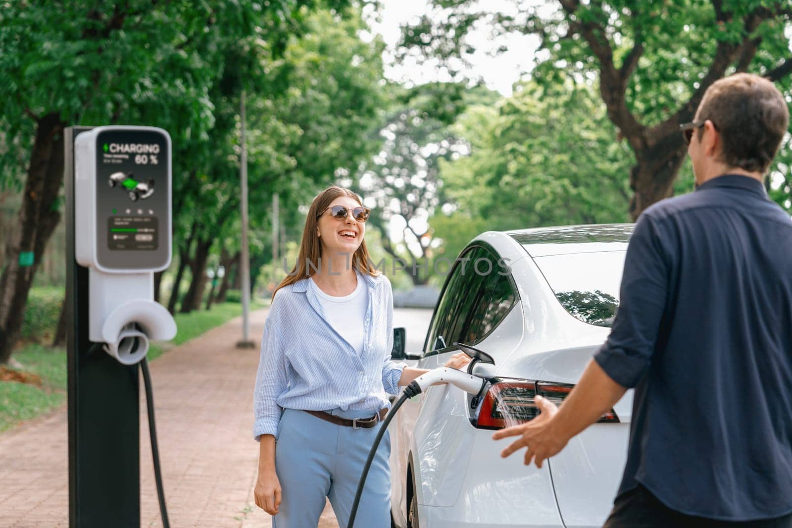 Lovely young couple recharging battery for electric car during road trip. Exalt by biancoblue