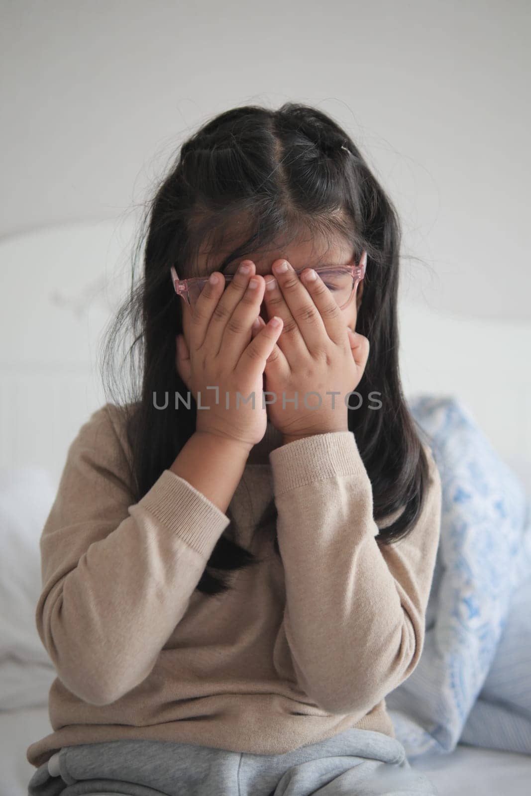 a upset child girl cover her face with hand .