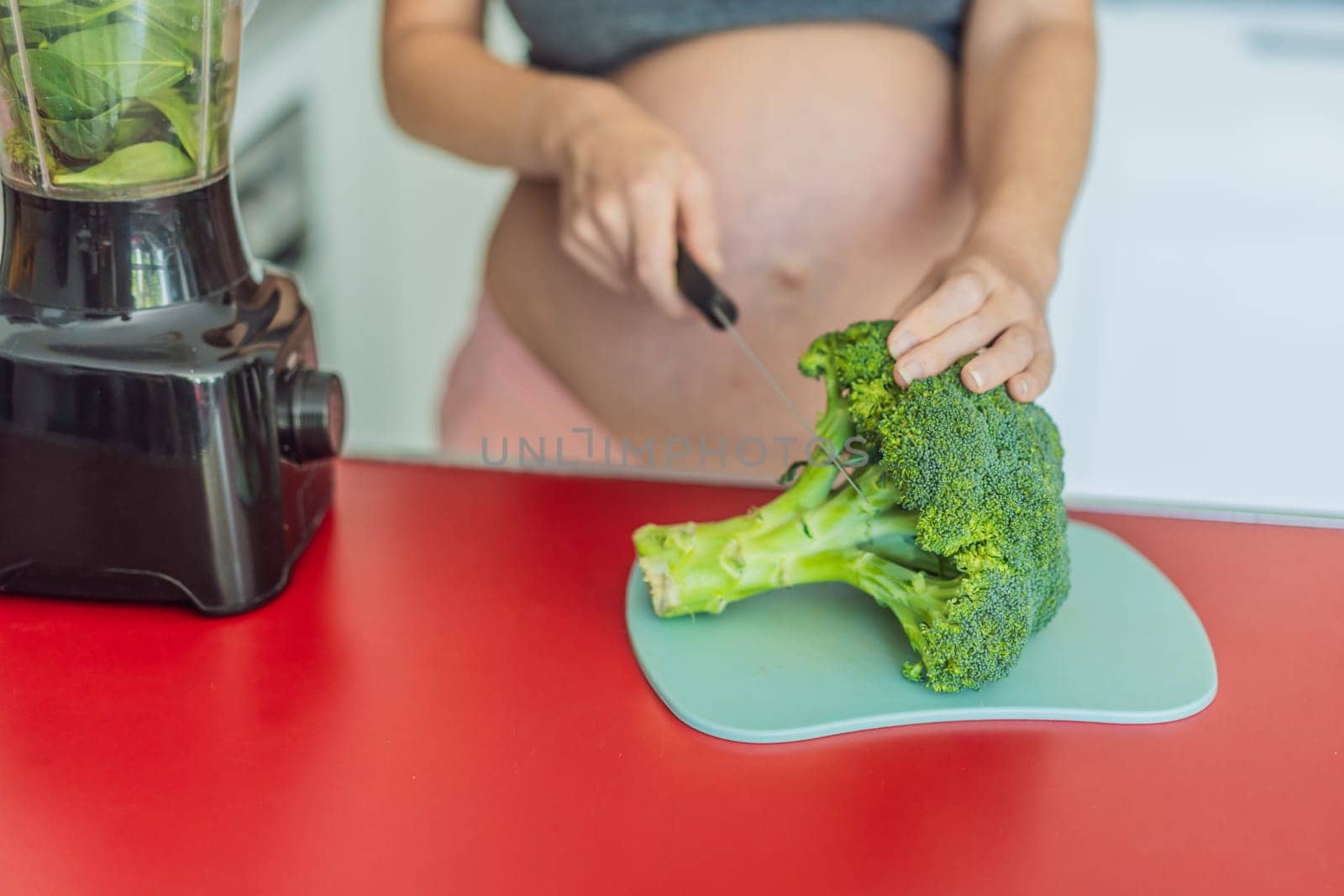 Embracing a nutritious choice, a pregnant woman joyfully prepares a vibrant vegetable smoothie, prioritizing wholesome ingredients for optimal well-being during her maternity journey.