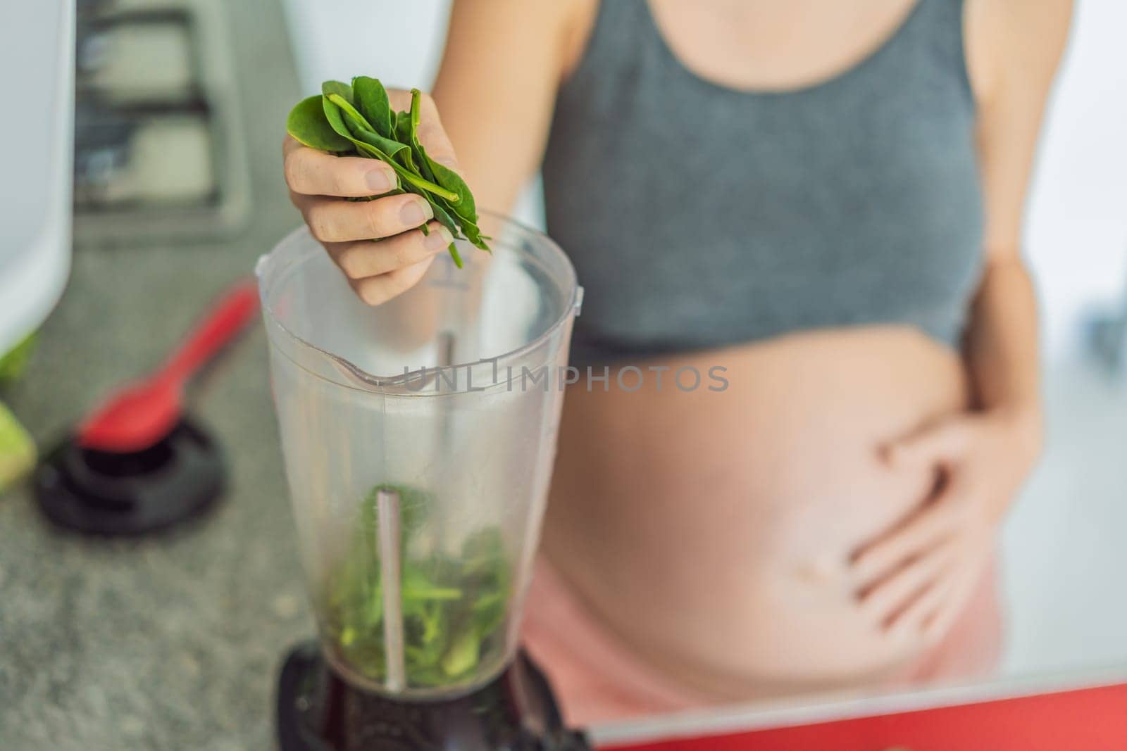 Embracing a nutritious choice, a pregnant woman joyfully prepares a vibrant vegetable smoothie, prioritizing wholesome ingredients for optimal well-being during her maternity journey by galitskaya