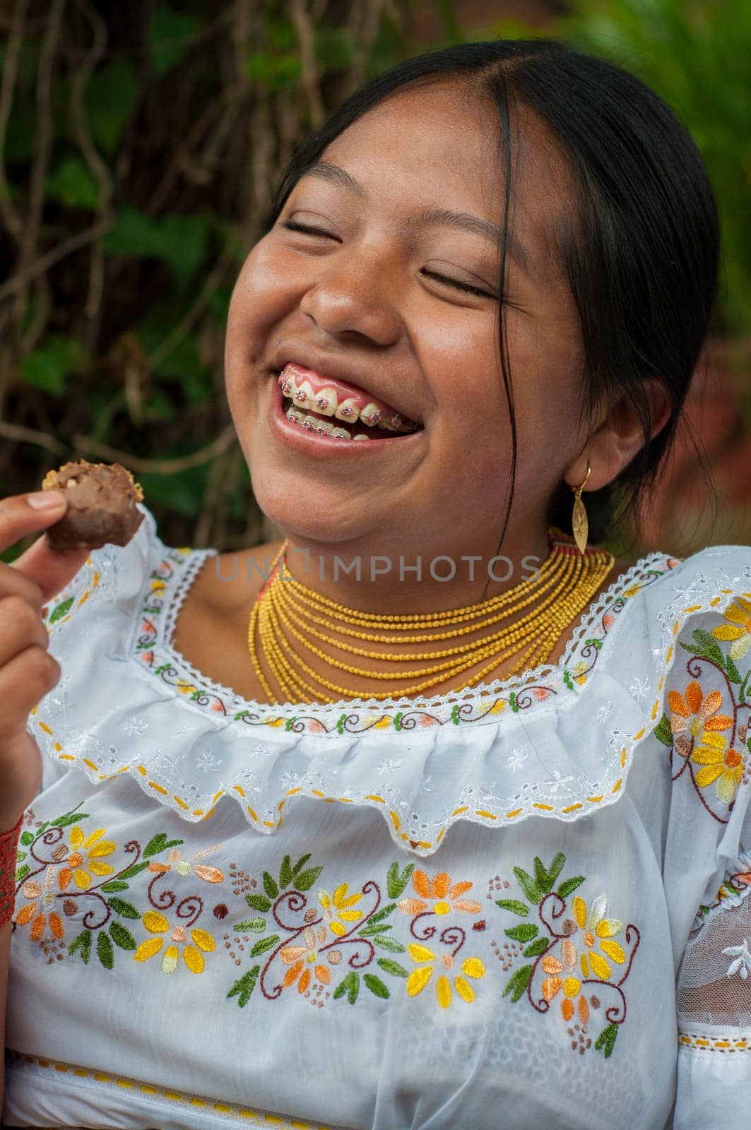 A cheerful young Indian girl with braces is captured in a moment of pure happiness as she enjoys a sweet treat outdoors, dressed in traditional embroidered clothing. High quality photo