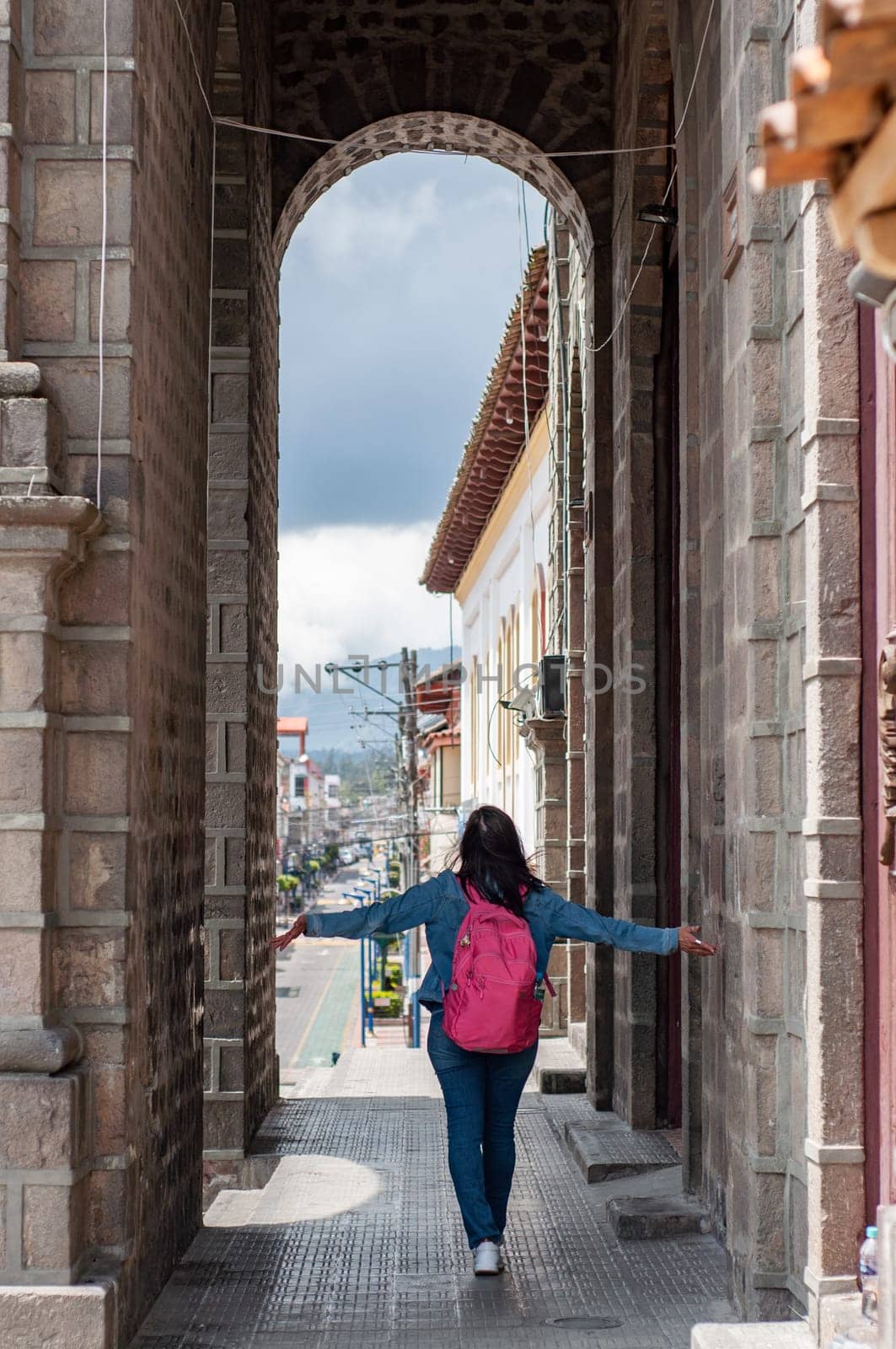 A pedestrian strolling under a pink archway amidst city buildings. by Raulmartin