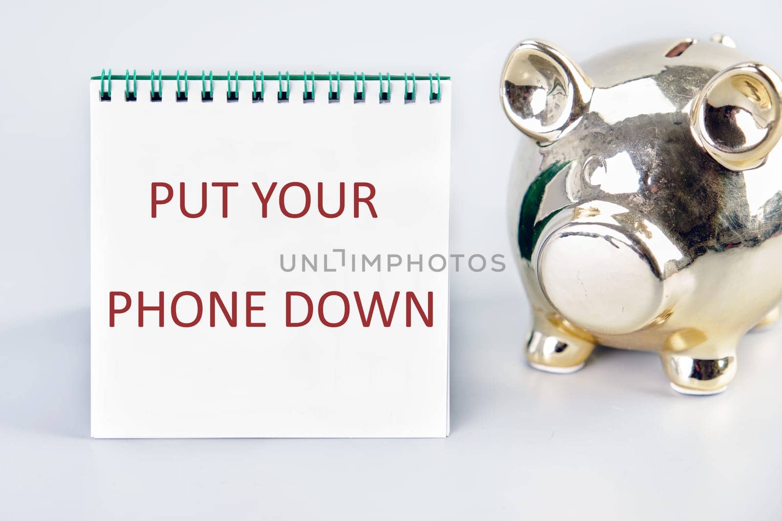 Put Your Phone Down text written on a notebook on a gray background next to a piggy bank