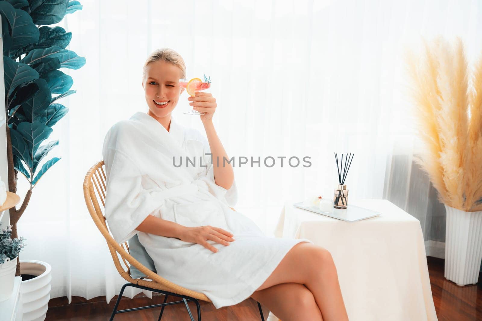 Beauty or body treatment spa salon vacation lifestyle concept with woman wearing bathrobe relaxing with drinks in luxurious hotel spa or resort room. Vacation and leisure relaxation. Quiescent