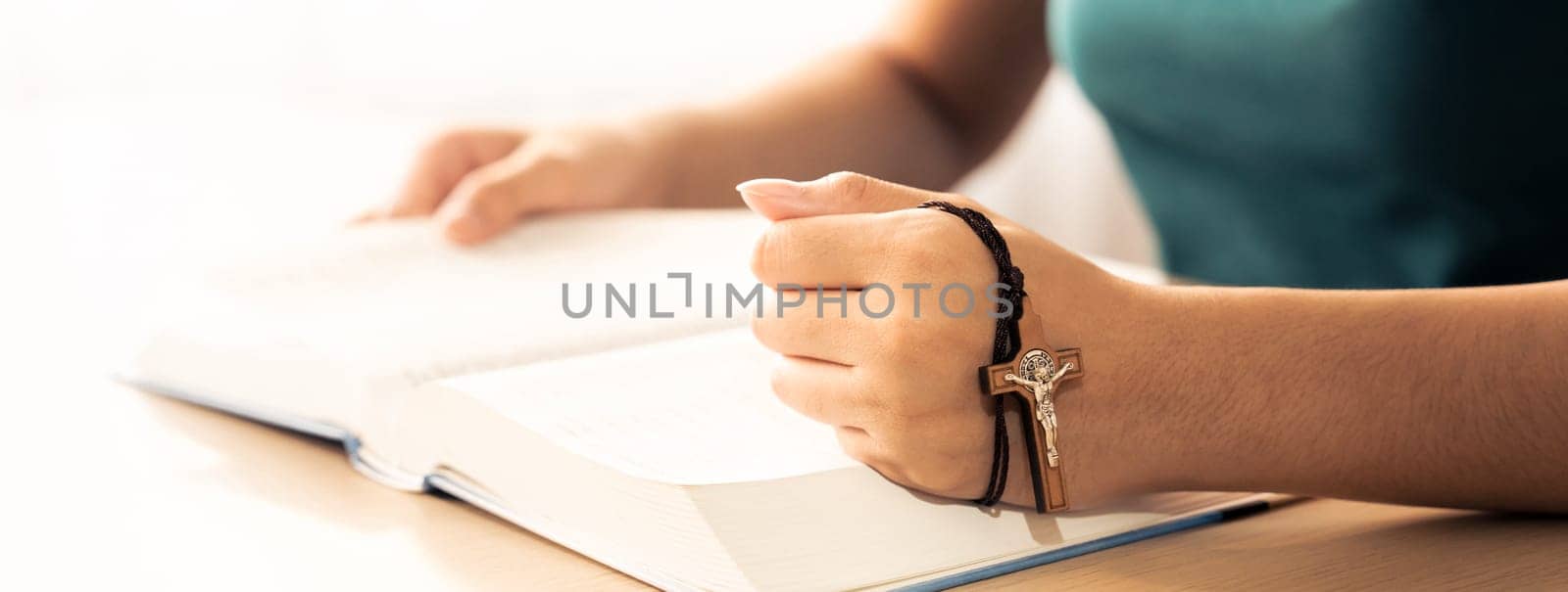 Cropped image of female reading a bible book while holding cross at wooden table with blurring background. Concept of hope, religion, faith, christianity and god blessing. Warm. Burgeoning.
