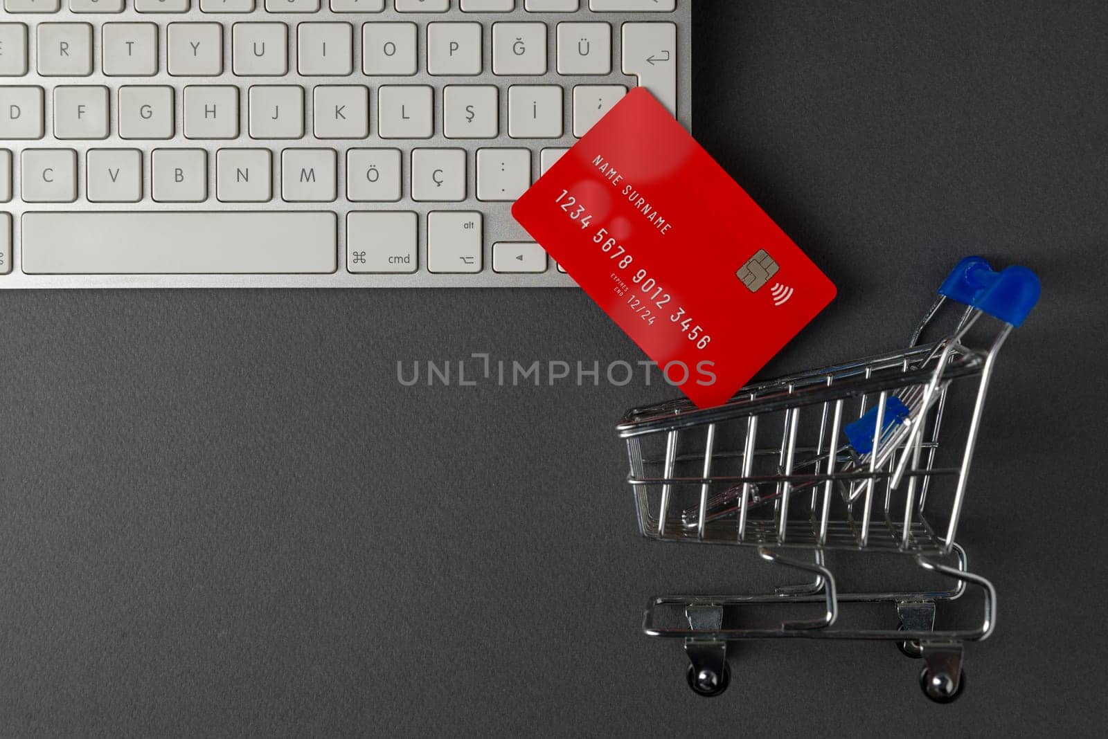 Top view of computer keyboard, credit card and mini market cart on dark gray table