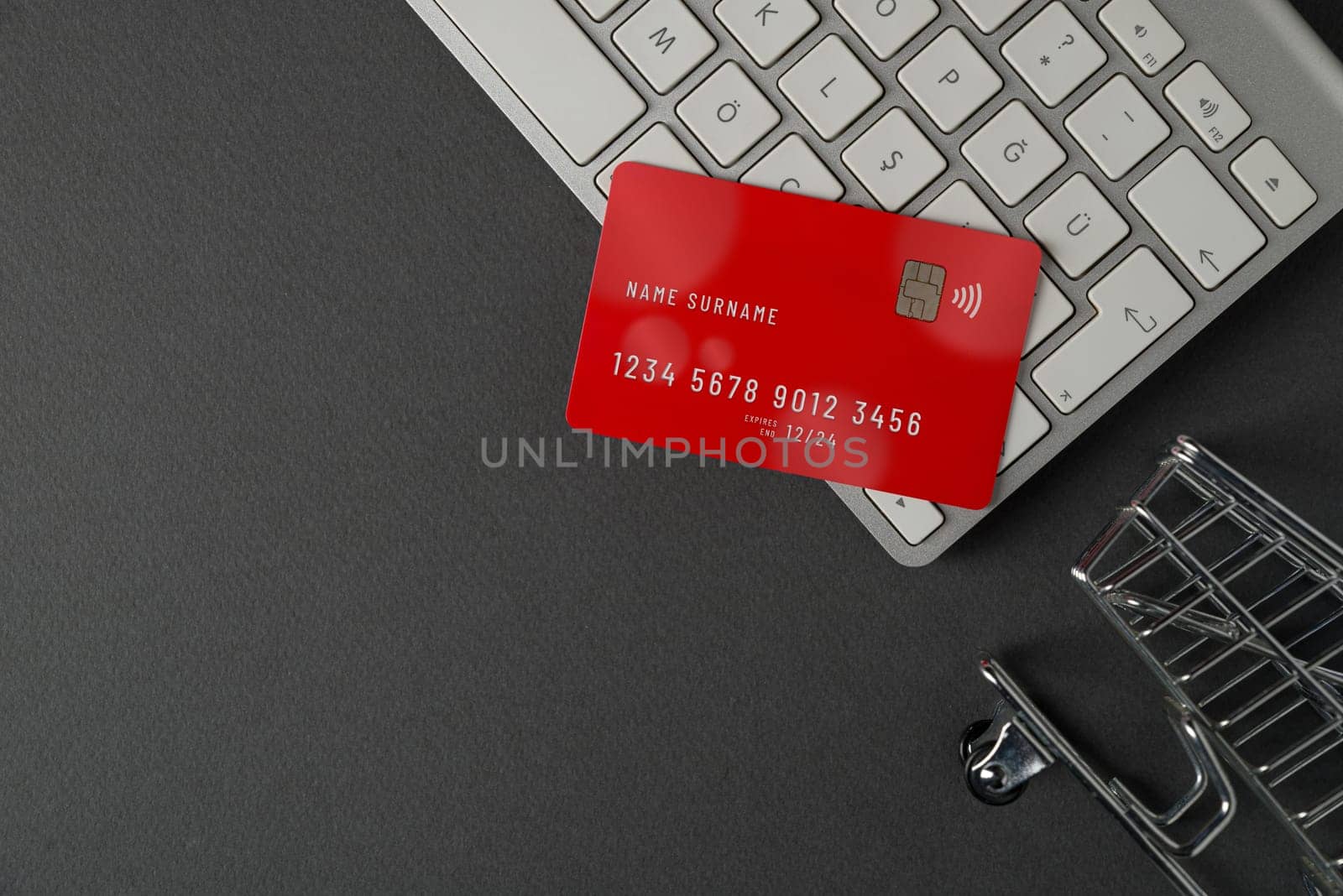 Top view of computer keyboard, credit card and mini market cart on dark gray table