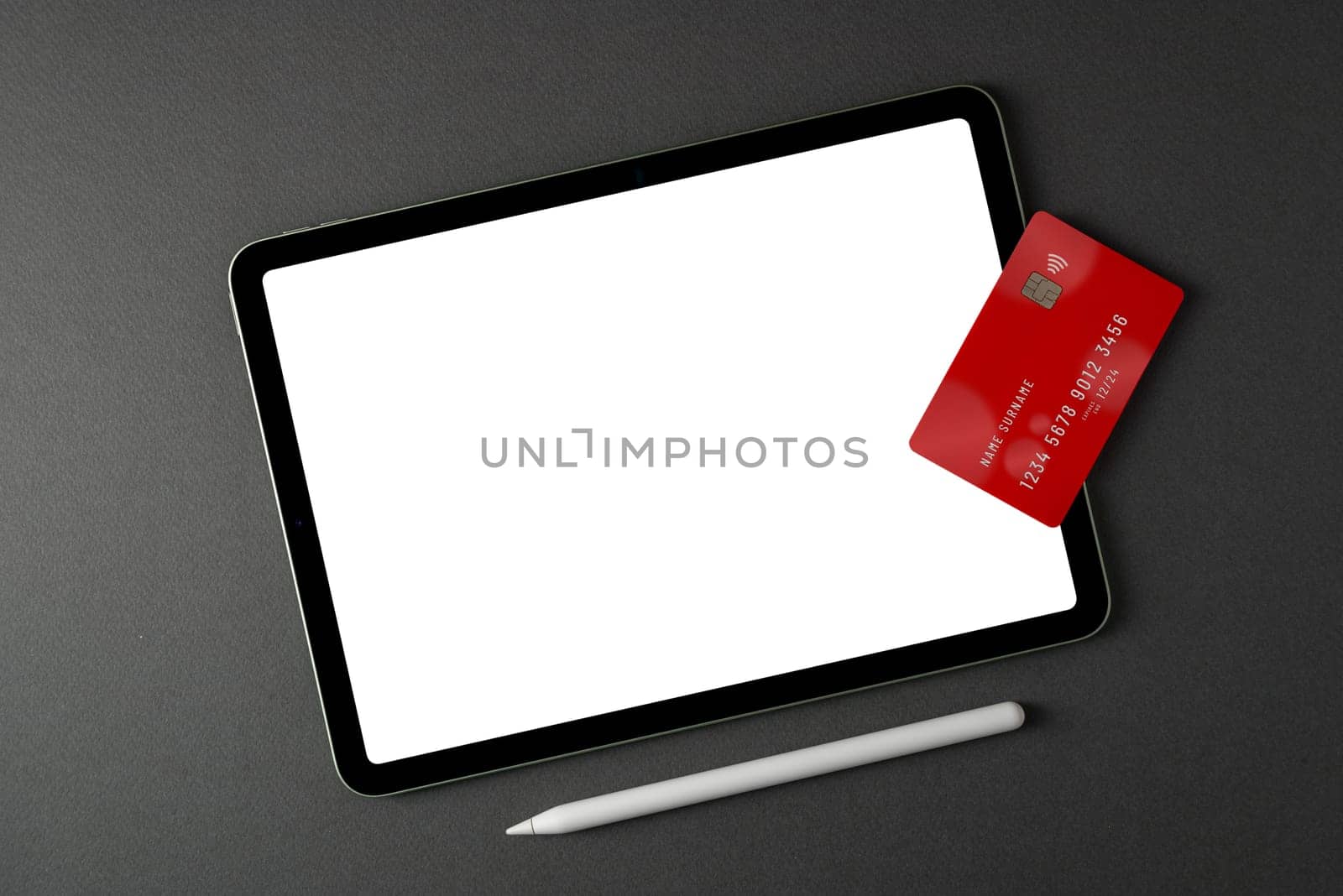 Credit card lying on tablet with blank screen on dark gray table