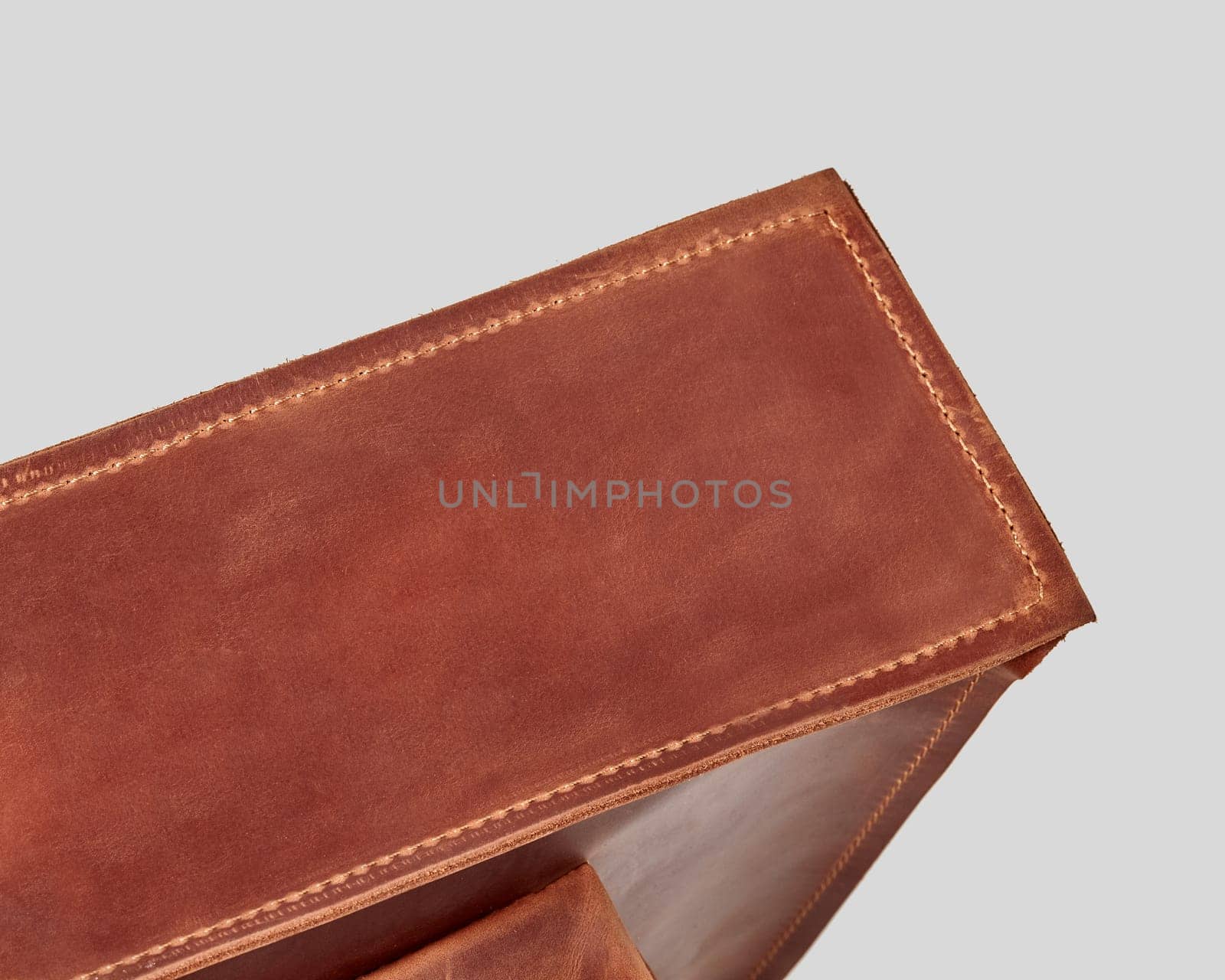 Detailed view of bottom of copper-colored genuine leather bag, highlighting texture of material and neat stitching. Concept of high-quality handicraft products