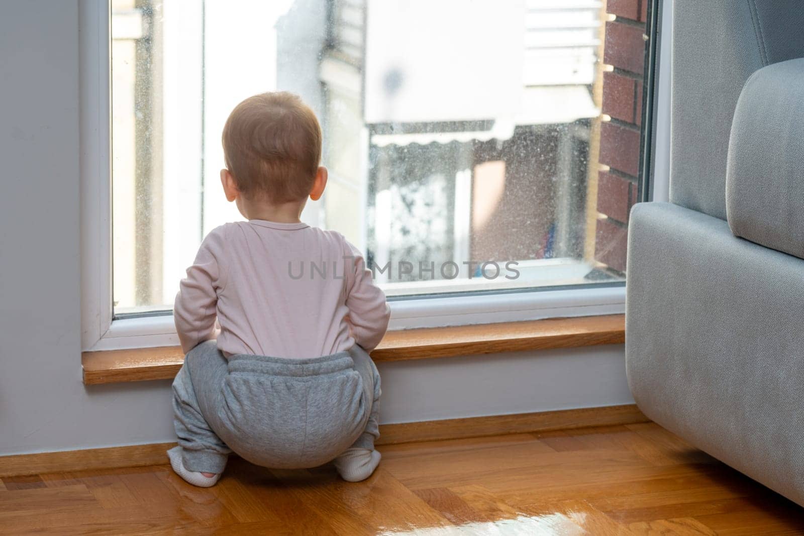 A toddler perches near a window in a home, looking out with longing for their father to come home from work. Concept of enduring love and the bond between child and parent