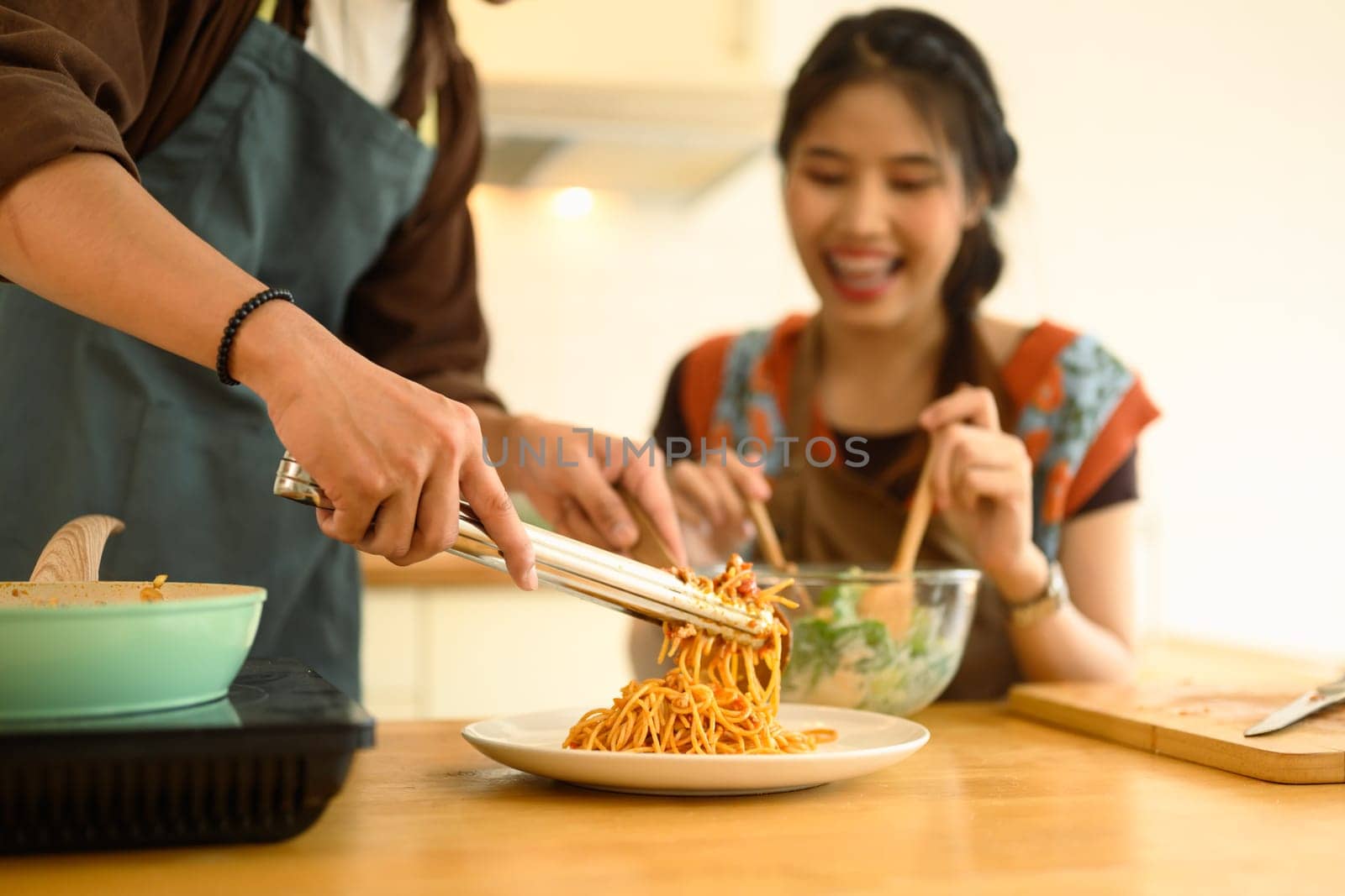 Happy couple enjoying lunch in the dinning room, man serving spaghetti bolognese. Love, relationships and food concept.