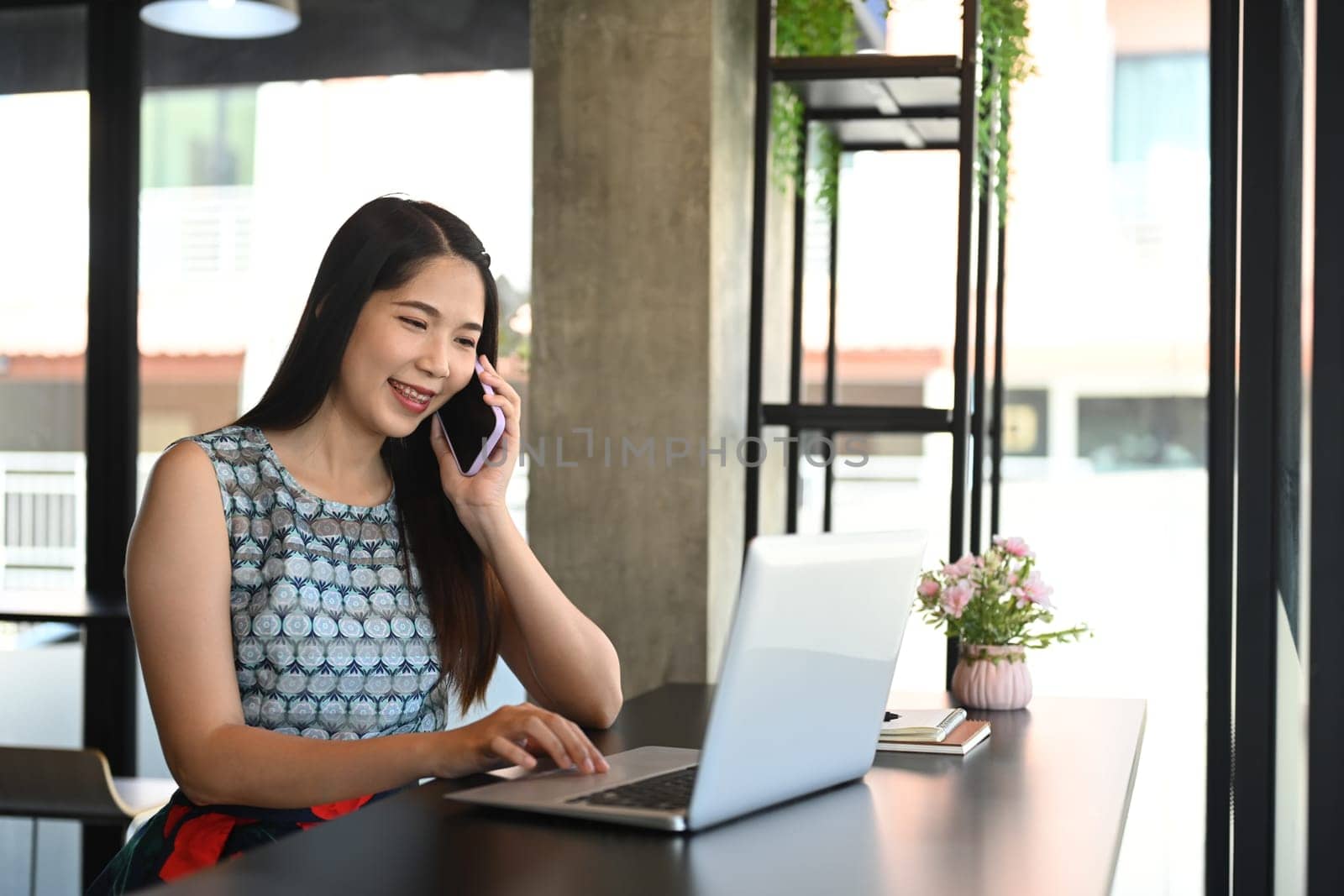 Attractive businesswoman having phone conversation and using laptop at bright office.