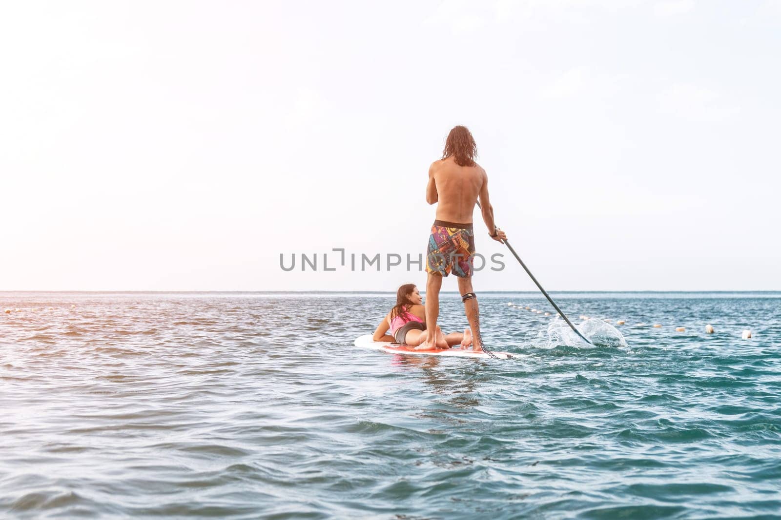 Sea woman and man on sup. Silhouette of happy young woman and man, surfing on SUP board, confident paddling through water surface. Idyllic sunset. Active lifestyle at sea or river