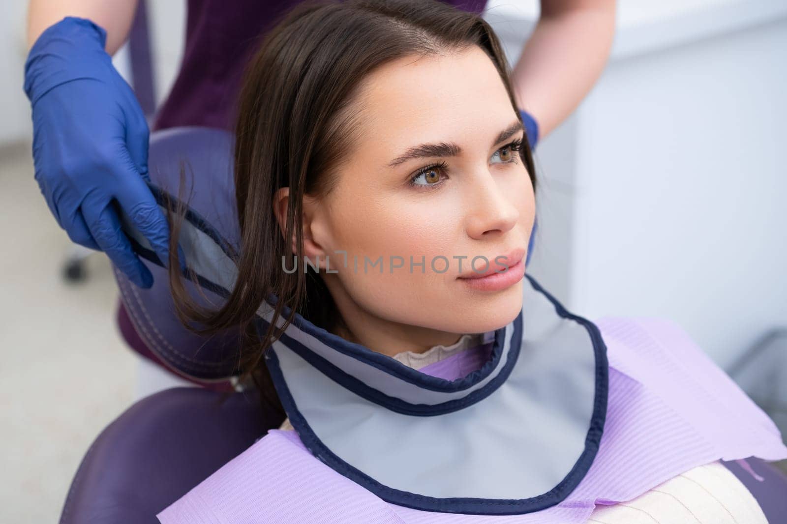 The dental assistant outfits the patient with a protective neck shield before commencing the tooth X-ray procedure.