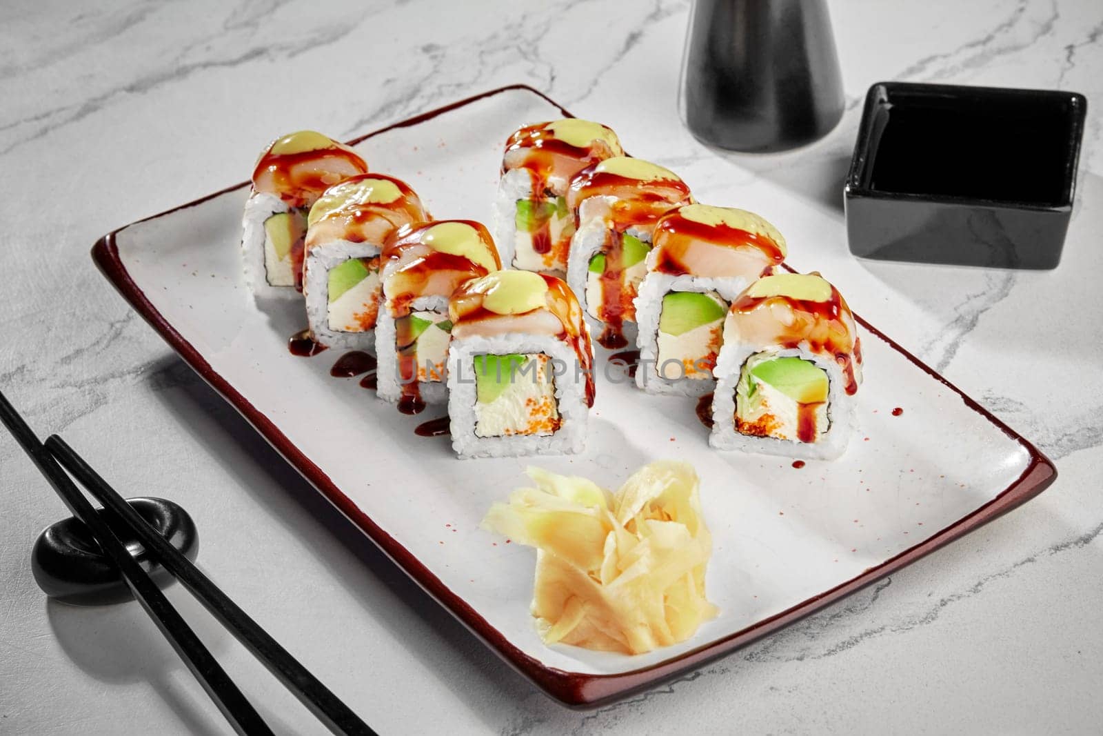 Appetizing sushi rolls with sea scallop, cream cheese, masago roe and avocado seasoned with spicy mayo an unagi sauce traditionally served with pickled ginger and soy sauce on plate