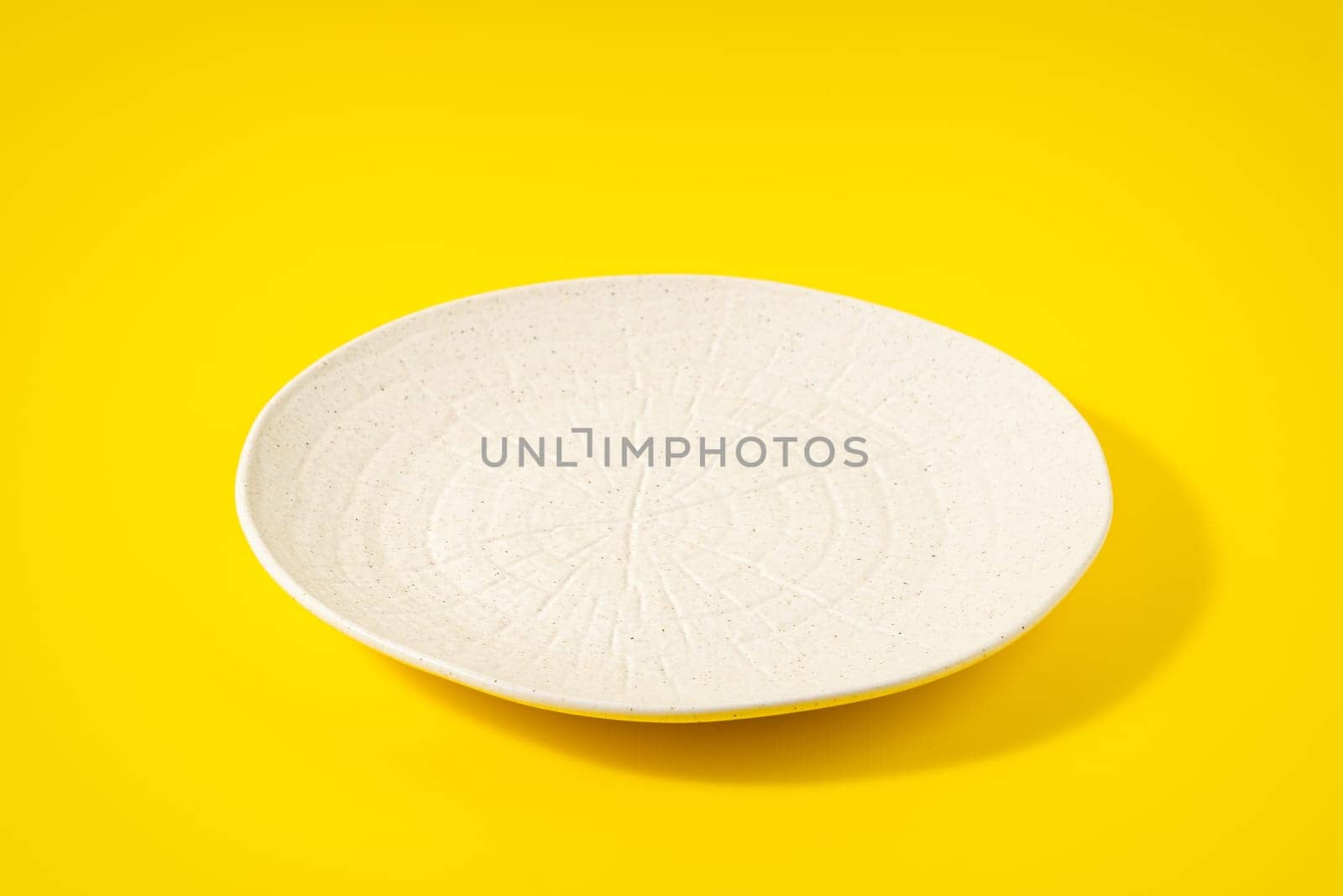 Empty white plate on a yellow background.