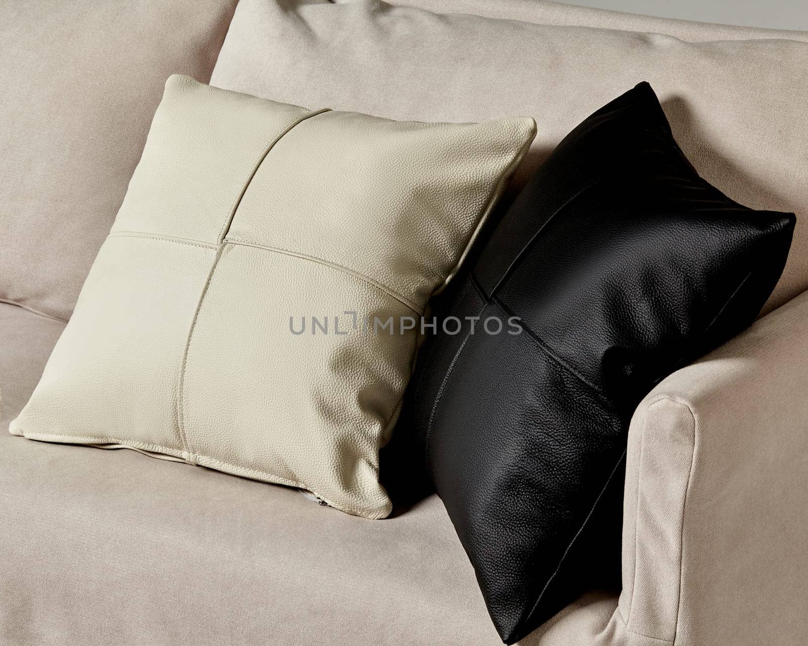 Close-up of cream and black leather pillows lying on neutral-toned sofa, showcasing simple sophisticated home style. Artisanal accessories for stylish interior