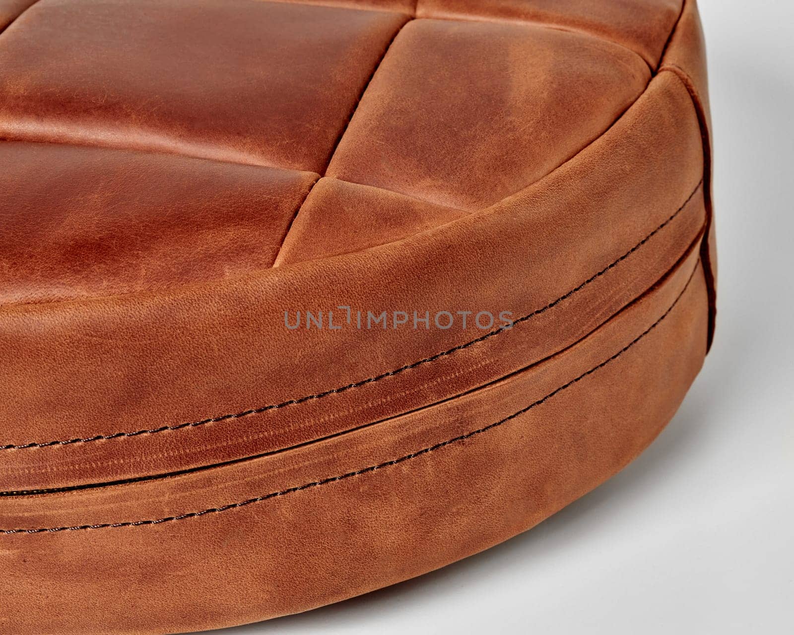 Close-up detailed view of brown leather patchwork floor cushion with neat stitching lines and hidden side zipper on white background. Artisanal interior design item