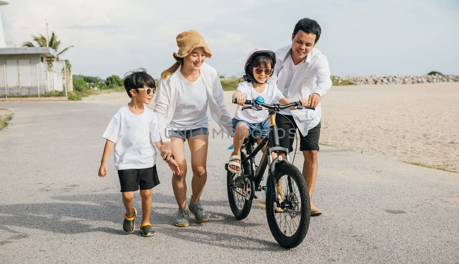 Summer fun by sea, Happy parents guide their children in learning to ride bicycles on a sandy beach. Smiles safety helmets and freedom of cycling characterize this cheerful tourism day concept. by Sorapop