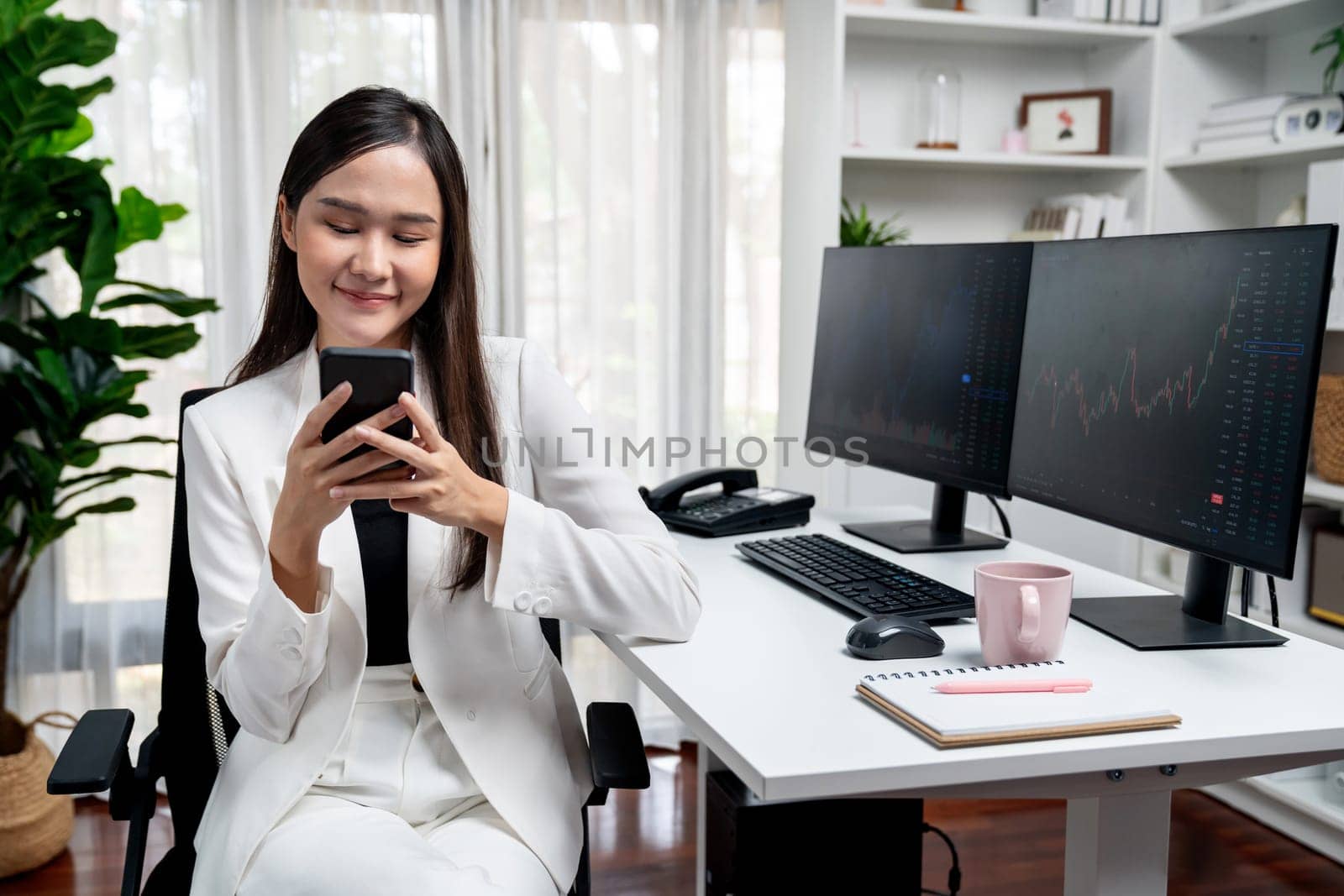 Smiling Asian businesswoman with happy face looking phone in stock. Stratagem. by biancoblue