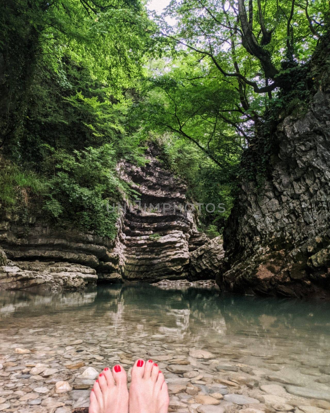 Woman feet with red pedicure in the background of rocks and caves and azure clear water and green trees. High quality photo