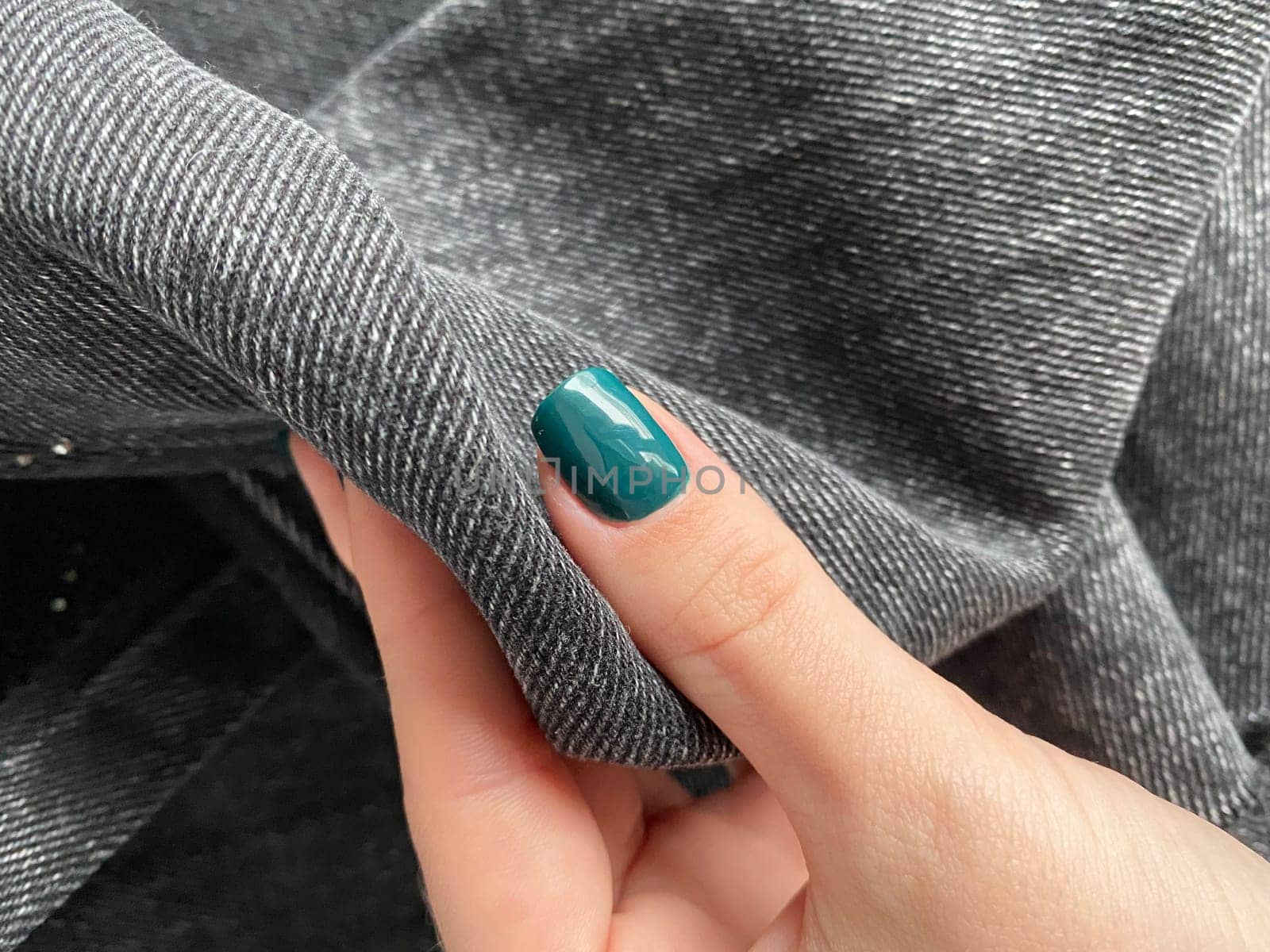 A woman's hand with a green nail polish on the background grey jeans . High quality photo