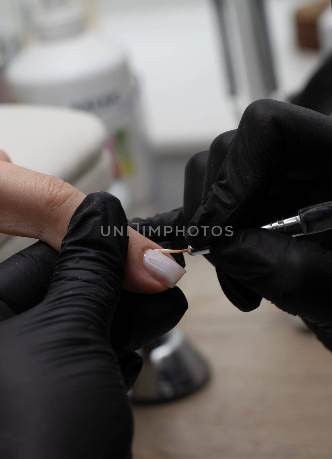 Beauty concept. A manicurist in black latex gloves makes a hygienic manicure and paints the client's nails with gel polish in a beauty salon. Close-up. Vertical.